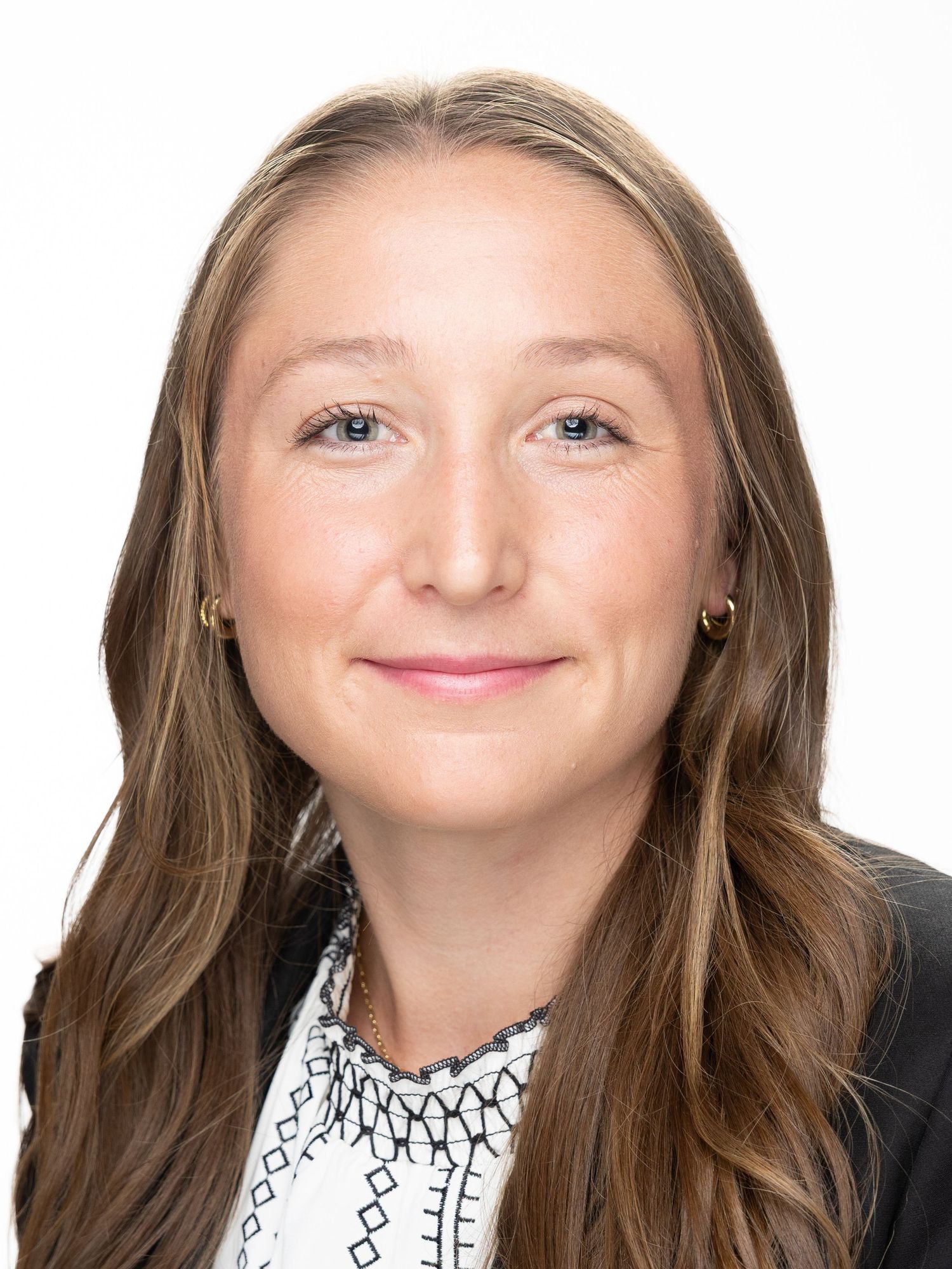Professional headshot of a young woman with long brown hair wearing a black blazer and white patterned top.