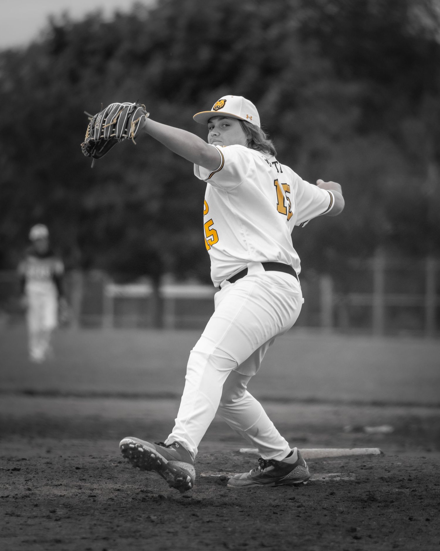 Baseball pitcher in white and gold uniform mid-windup on mound, selective color photo highlighting player against B&W background.