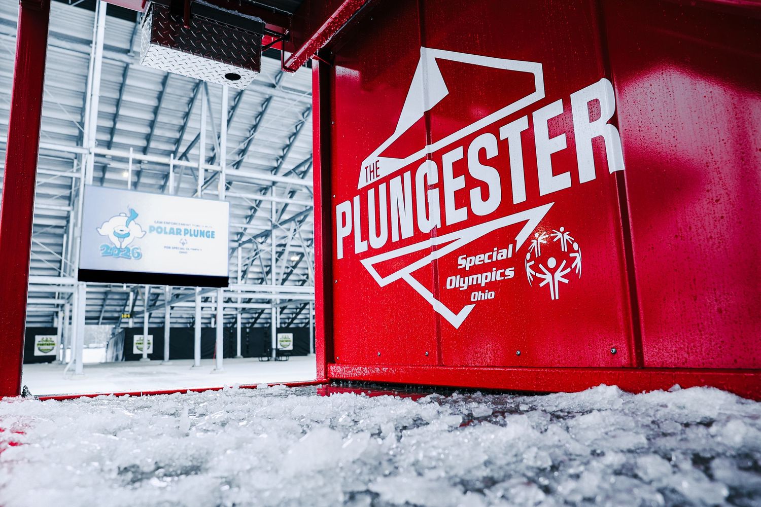 Red Plungester Special Olympics Ohio sign covered in snow outside a winter polar plunge event venue.