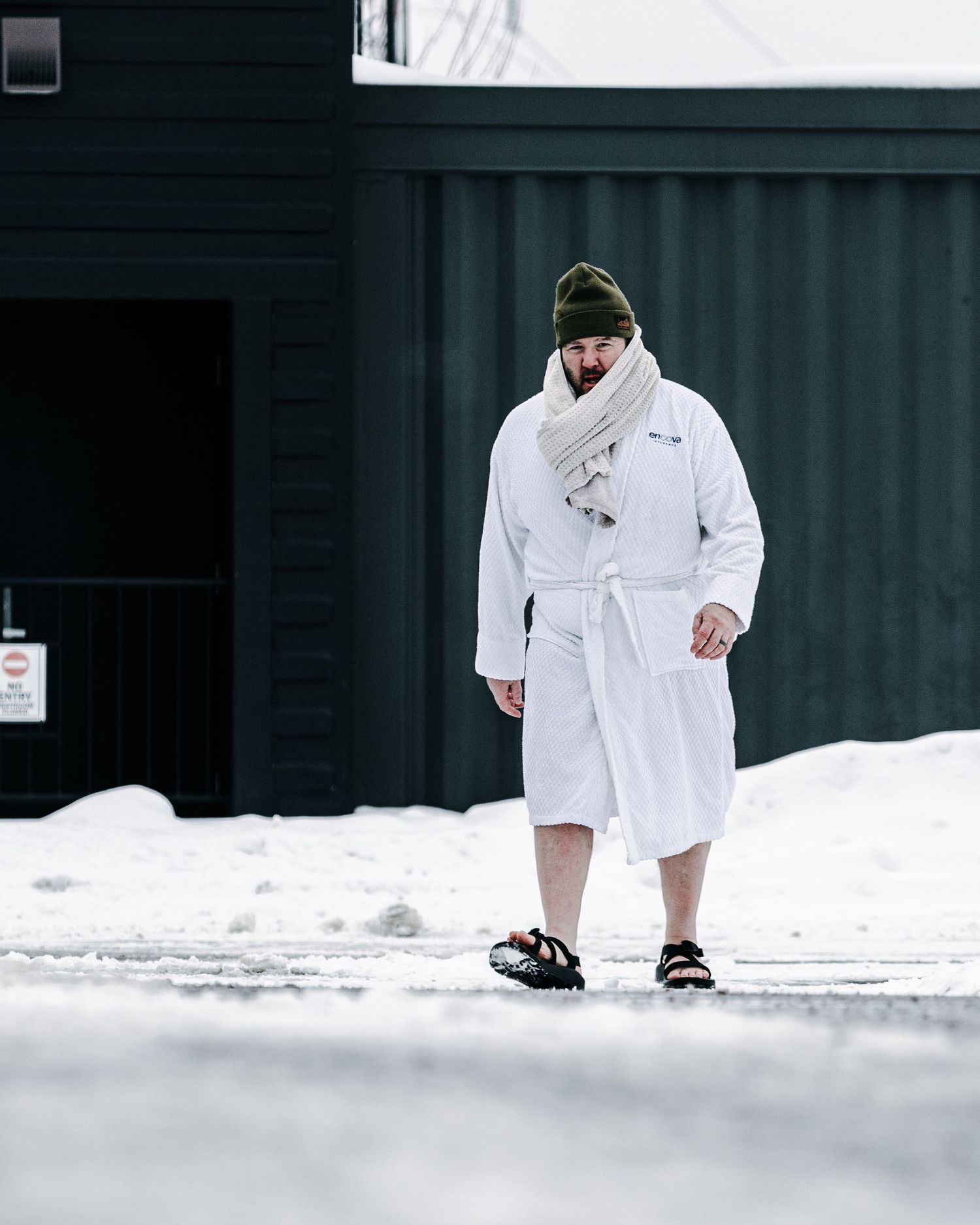 Man in white robe, scarf, and sandals walking in snowy outdoor setting wearing olive beanie hat.