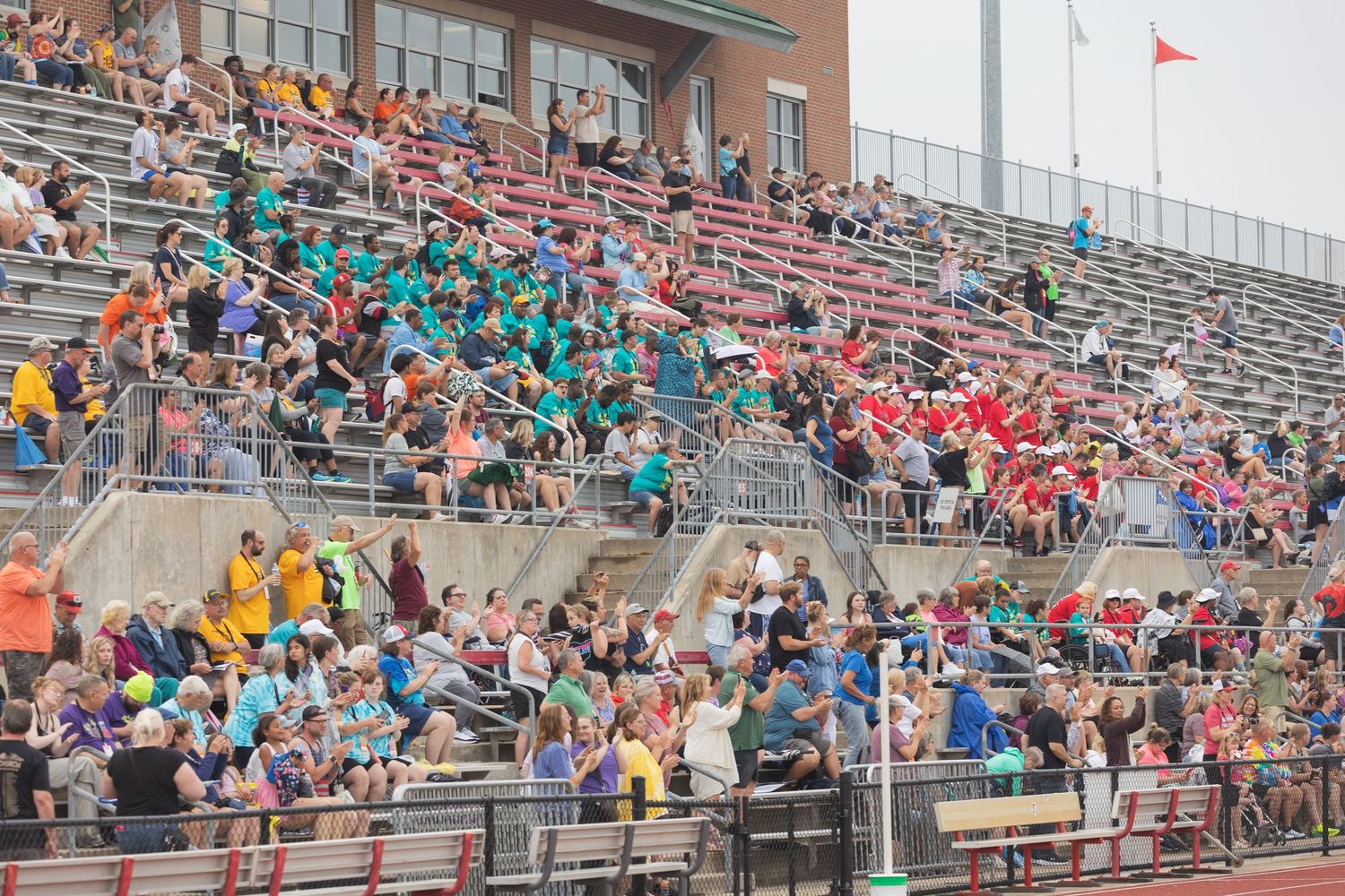 Large crowd of colorful Special Olympics spectators and athletes fill stadium bleachers during an outdoor track event.