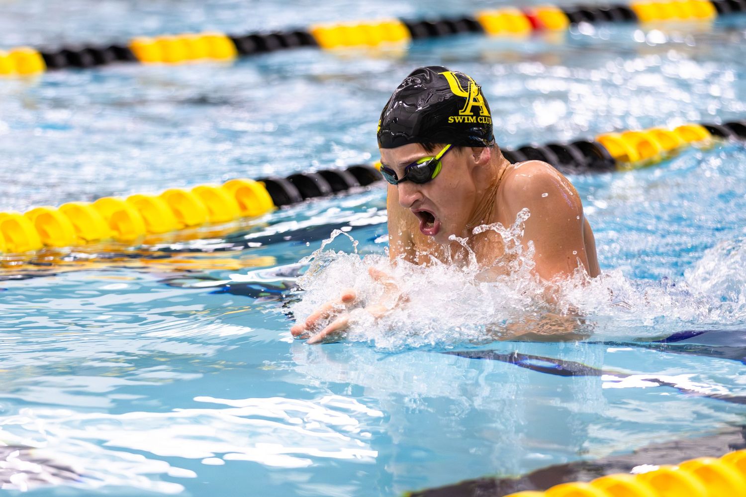 Competitive swimmer performing breaststroke in a pool, wearing a black cap and goggles, with yellow lane dividers.