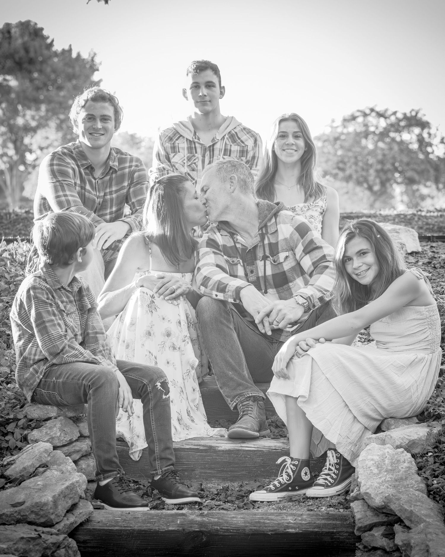Black and white family portrait of six children sitting and standing on stone steps outdoors among trees.