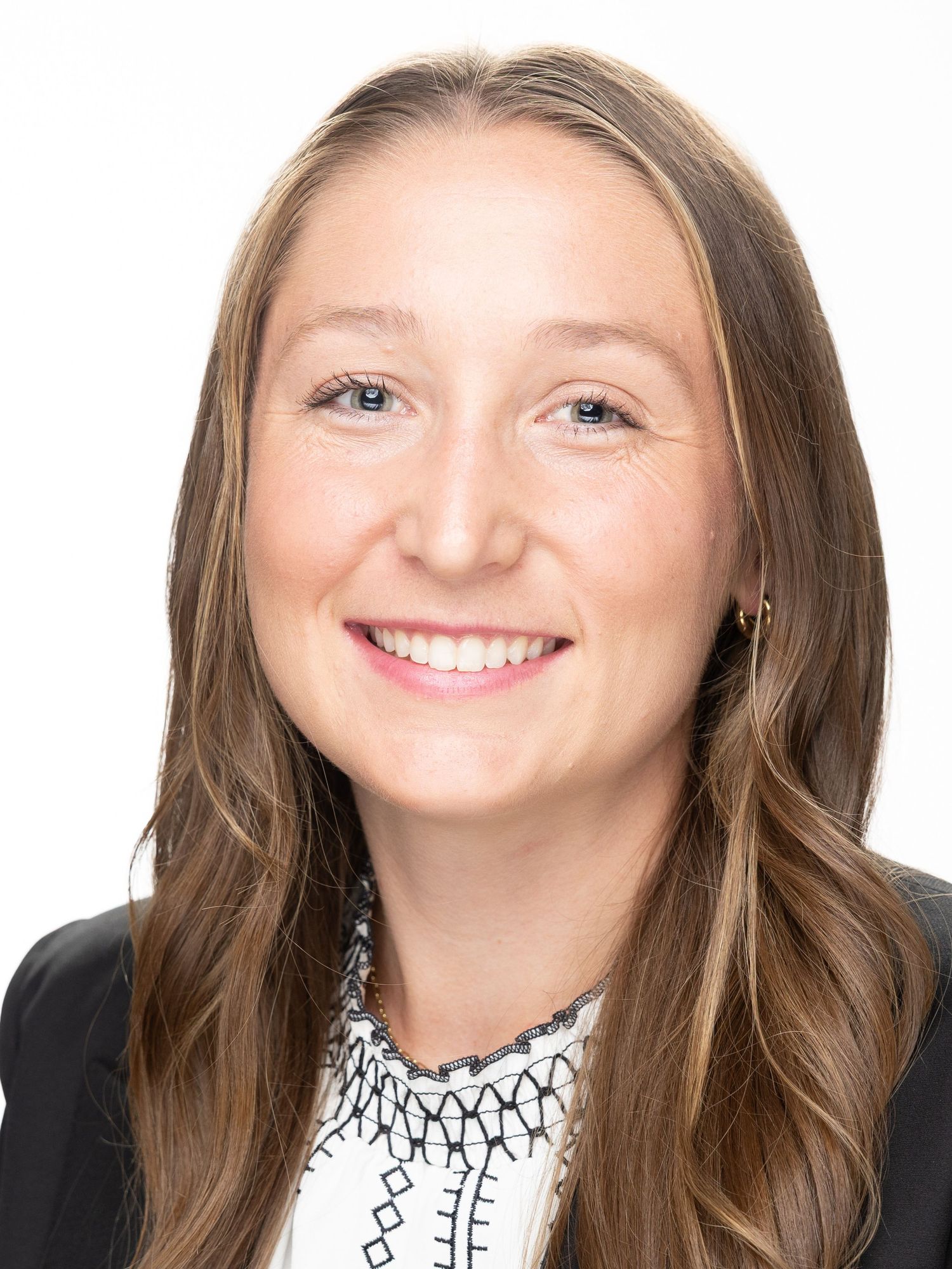Professional headshot of a smiling young woman with long brown hair wearing a black blazer and patterned blouse.