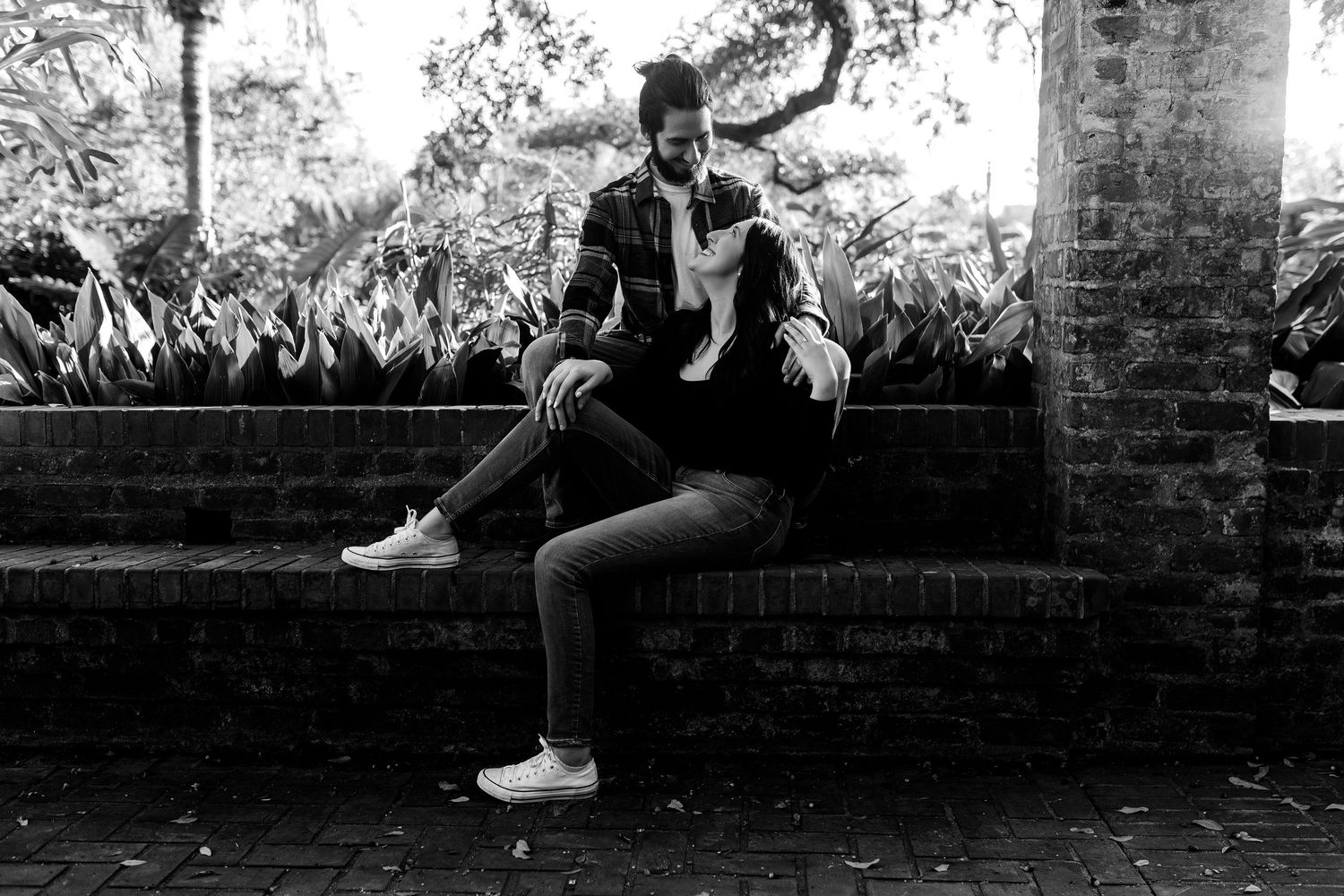A black and white photograph of a person sitting on a brick wall wearing a leather jacket and sneakers.