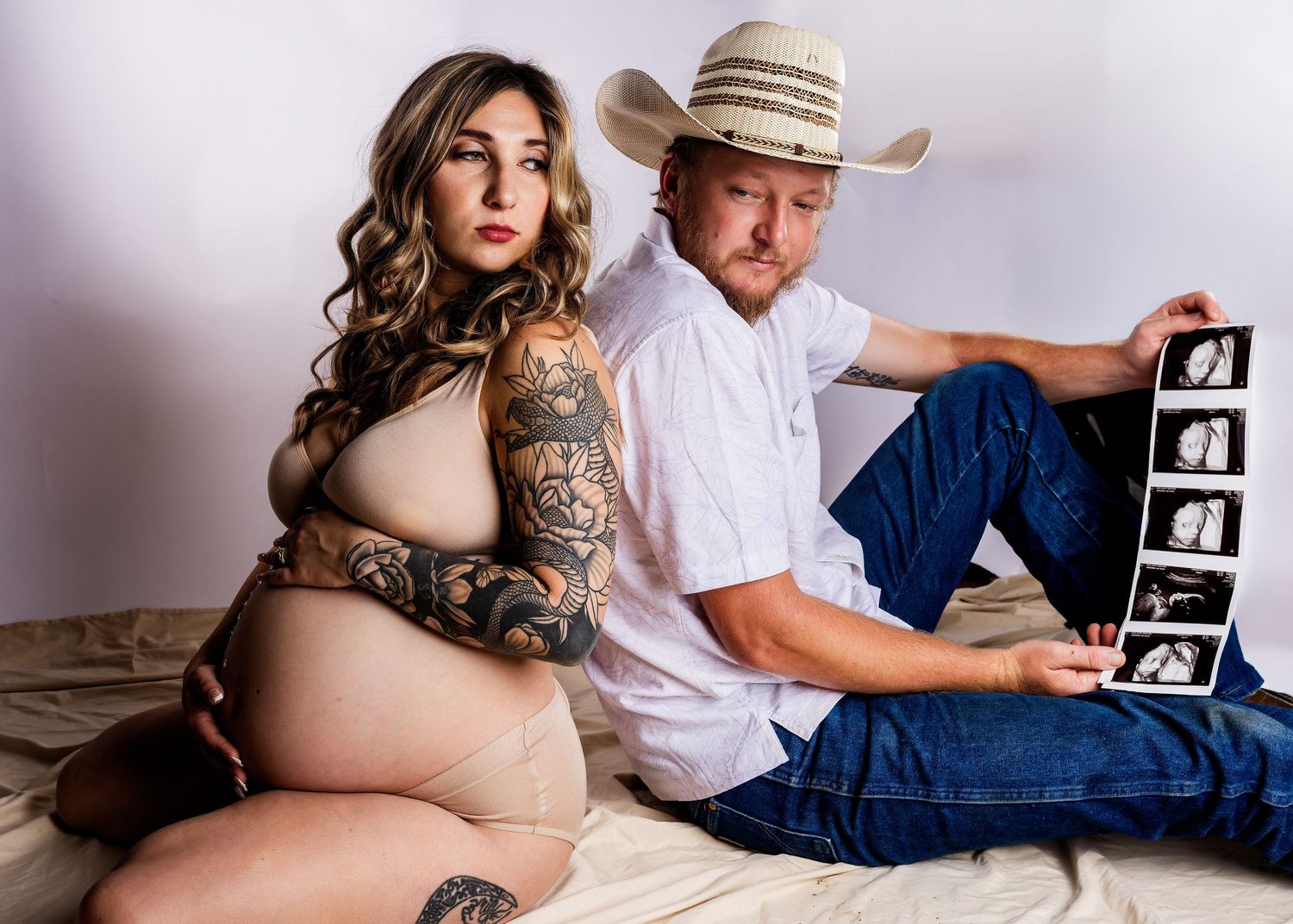 Couple poses on bed with ultrasound photos, expecting parents share intimate pregnancy announcement moment.