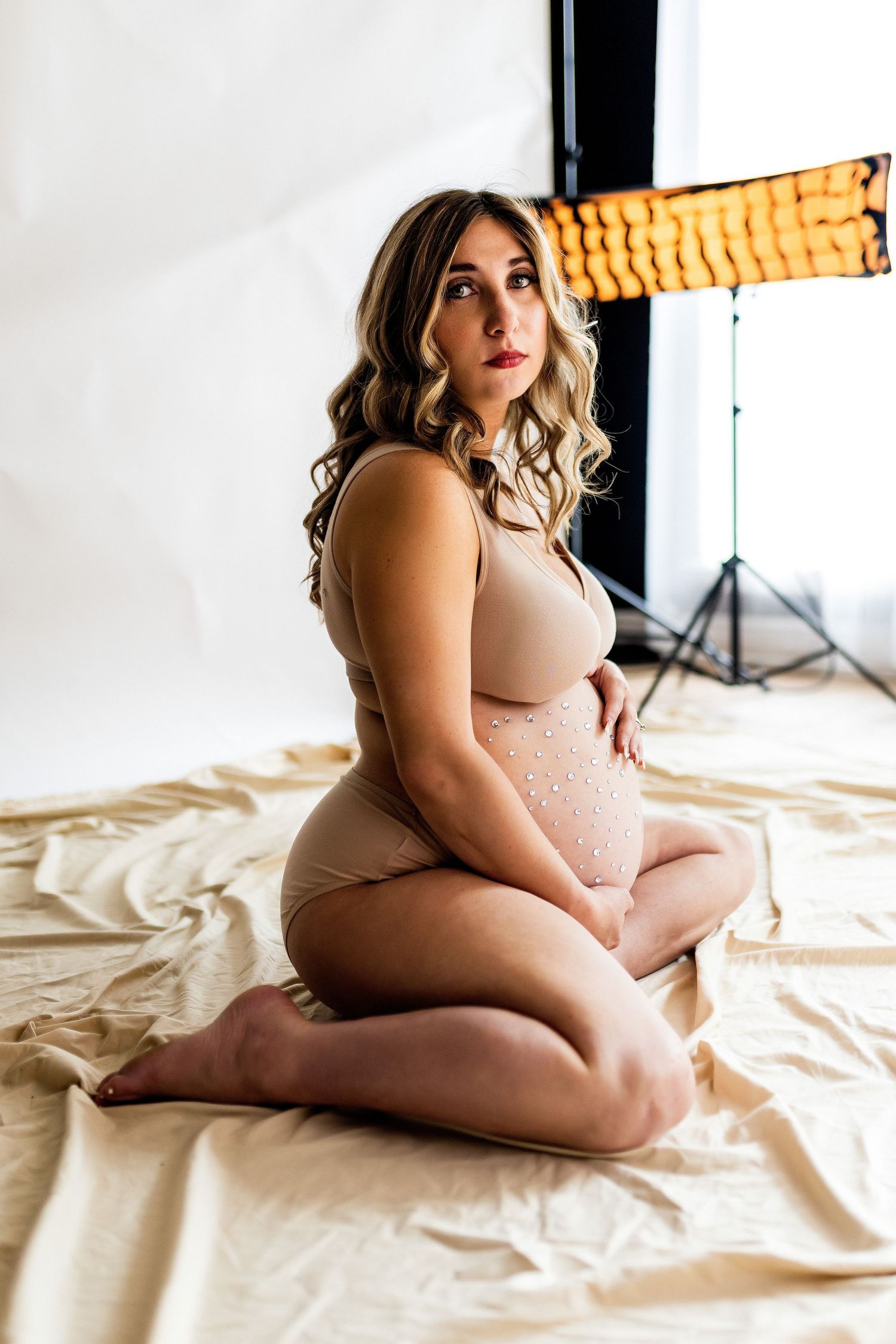 Body positive boudoir photo in warm lighting with beige lingerie on cream colored fabric.