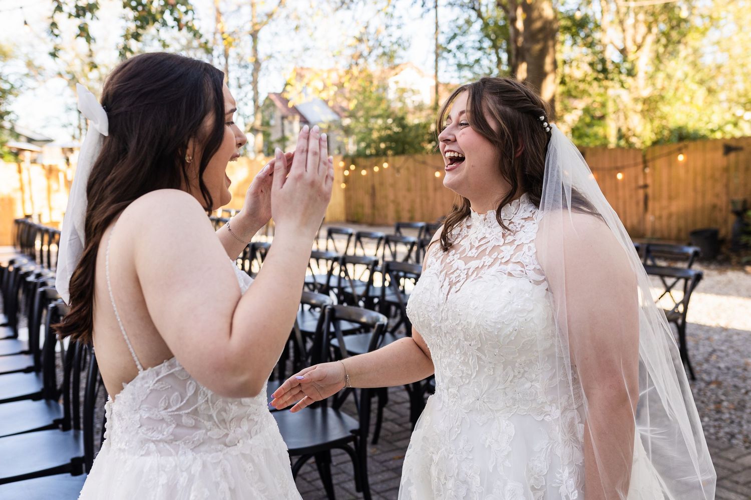Happy couple laughing and dancing together during outdoor wedding reception in sunlit garden setting.