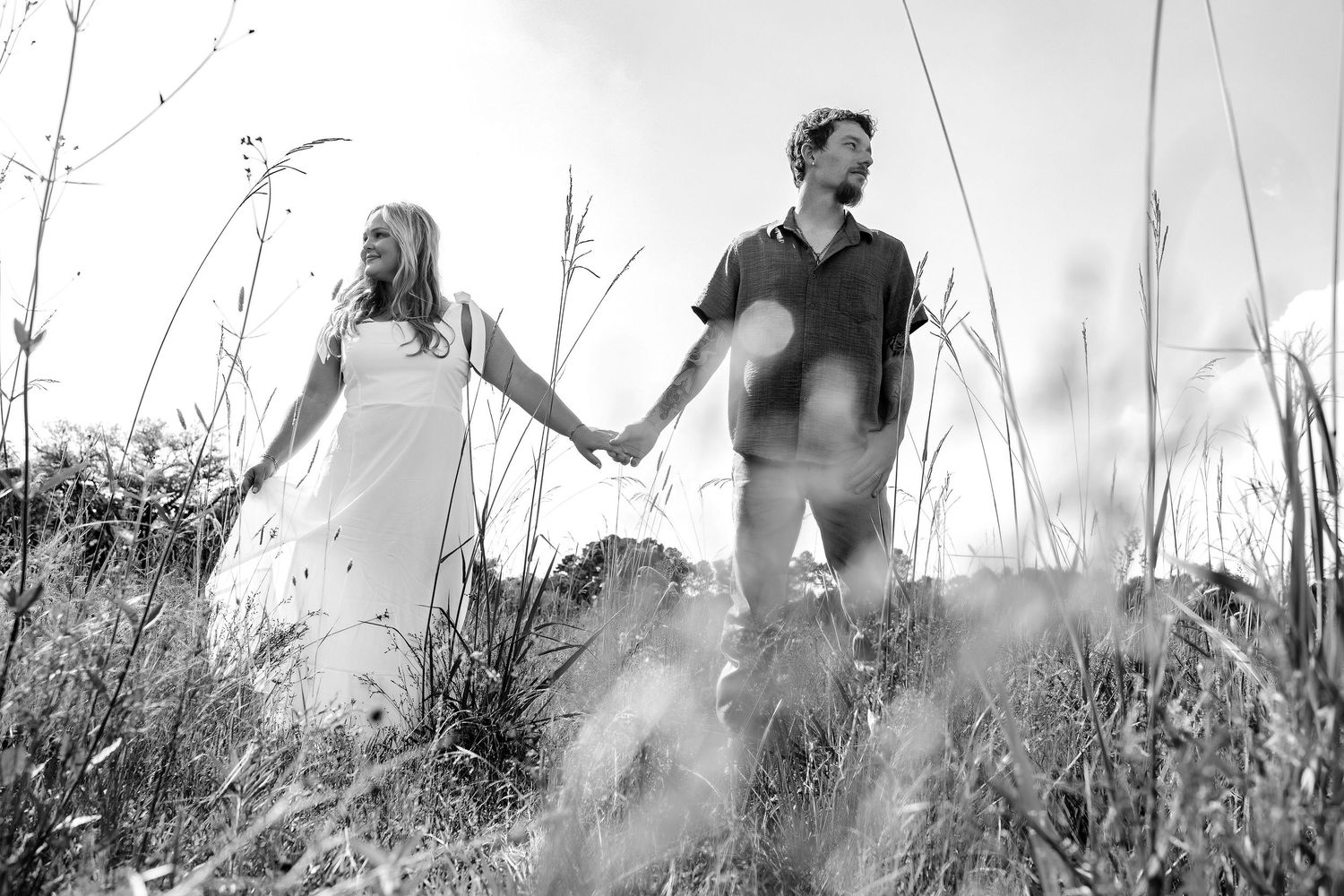Silhouetted figures walk through tall grass in a dreamy black and white scene.