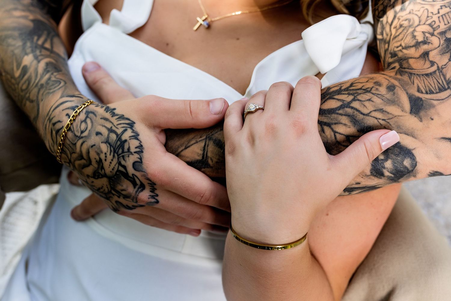 Detailed view of tattooed hands gently touching with delicate jewelry accents.