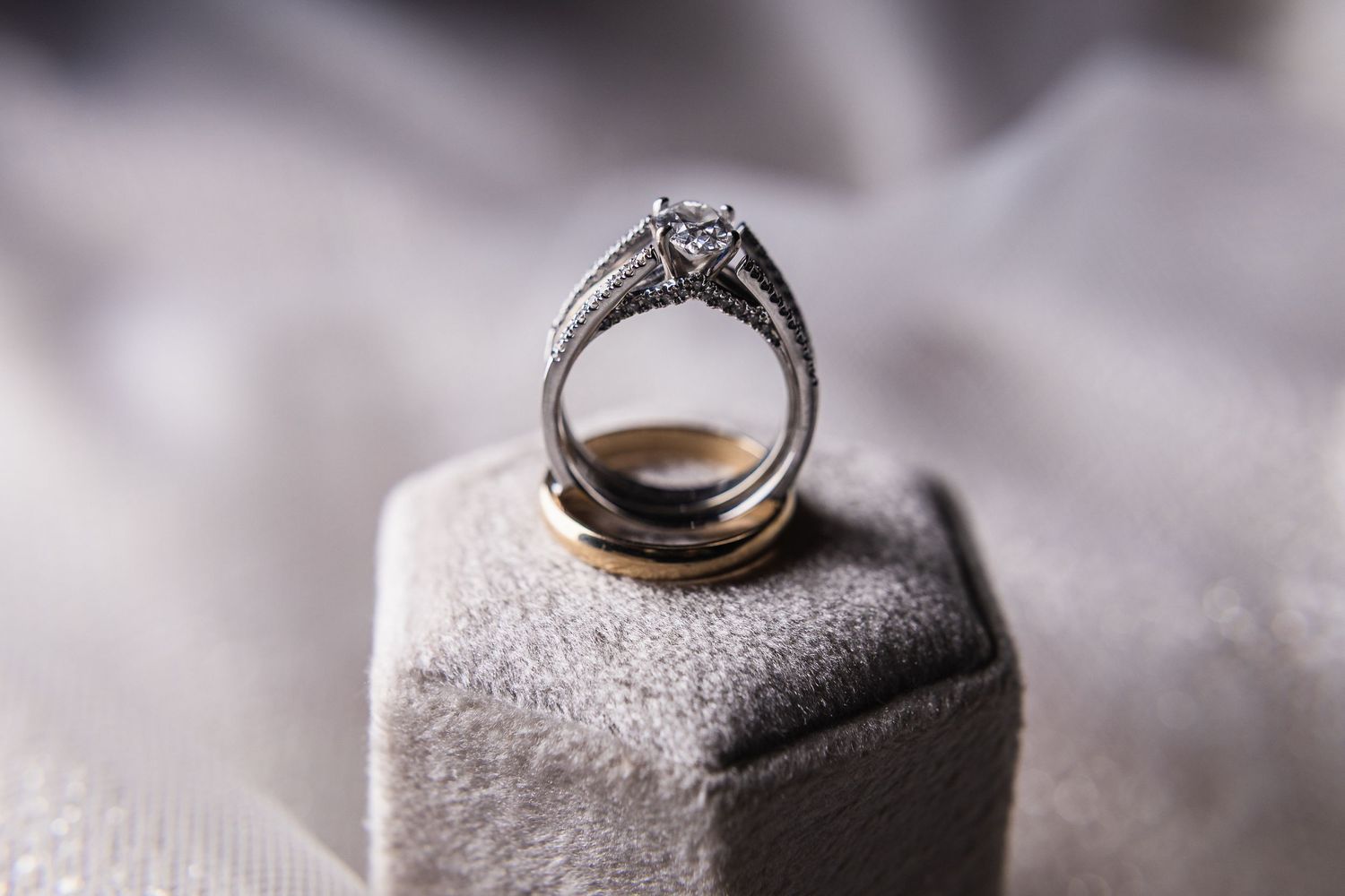 A diamond engagement ring sits elegantly on a gray velvet display stand with soft lighting and shallow depth of field.