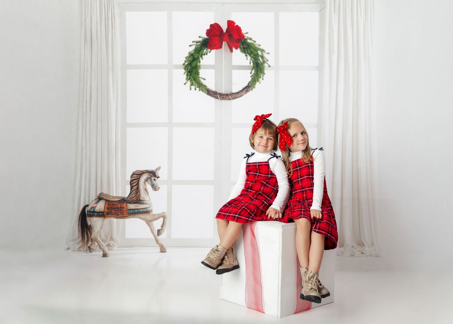 Two matching red sequin holiday dresses with a wooden rocking horse and Christmas wreath in white room setting.
