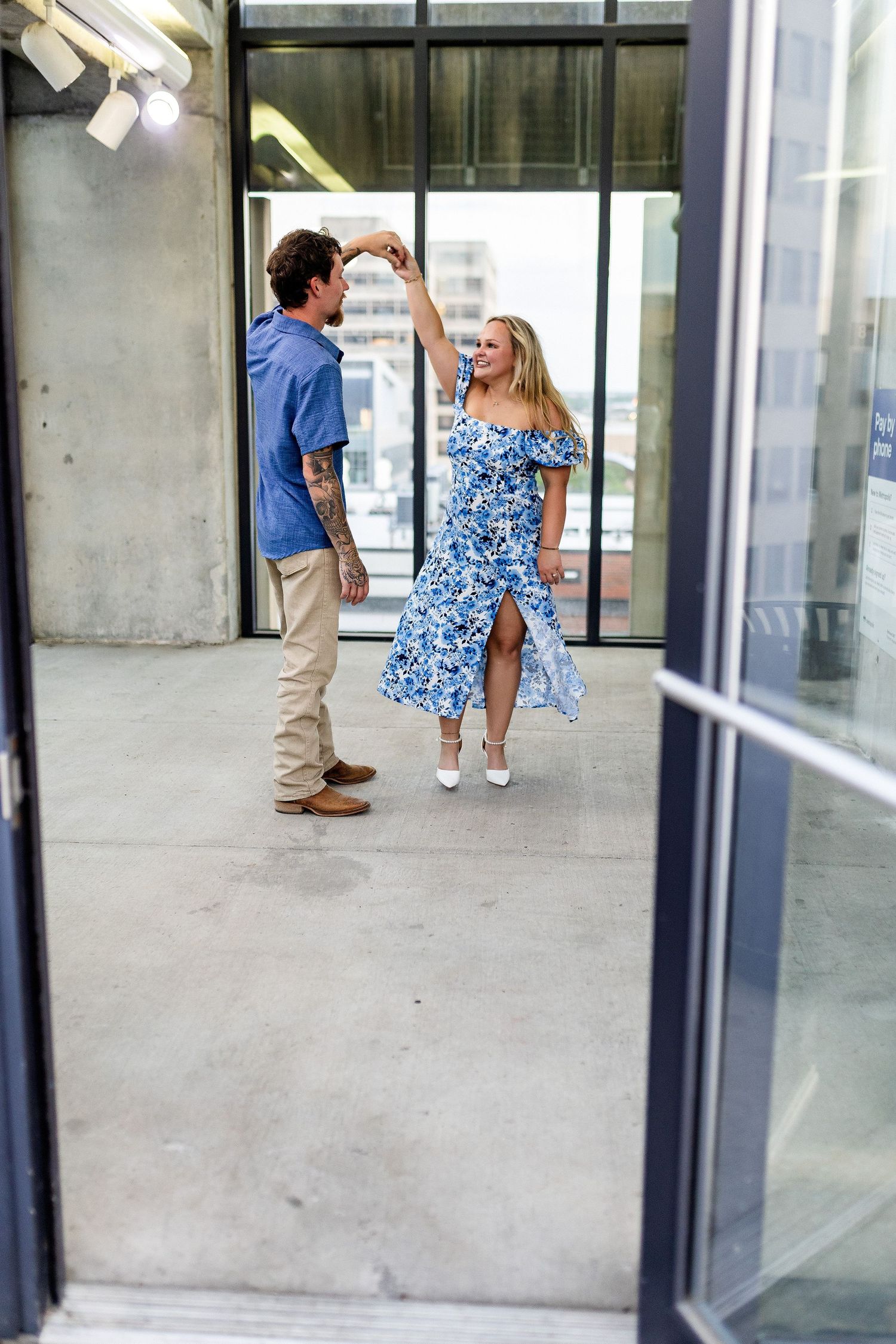 People in blue floral dresses walking near glass doors and concrete pillars in a modern building hallway.