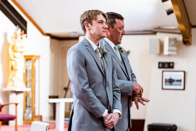 A tender moment shared between two people in gray suits during a wedding ceremony.