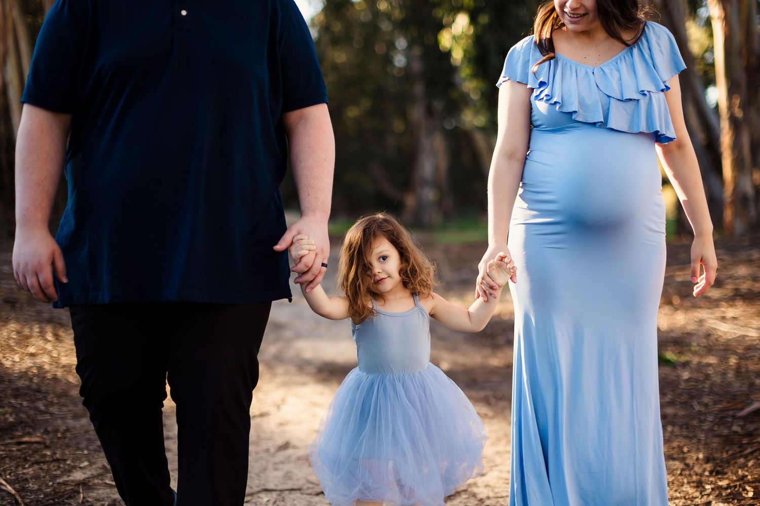 Romantic outdoor couple photoshoot featuring light blue bridesmaid dresses and formal black attire in a forest setting.