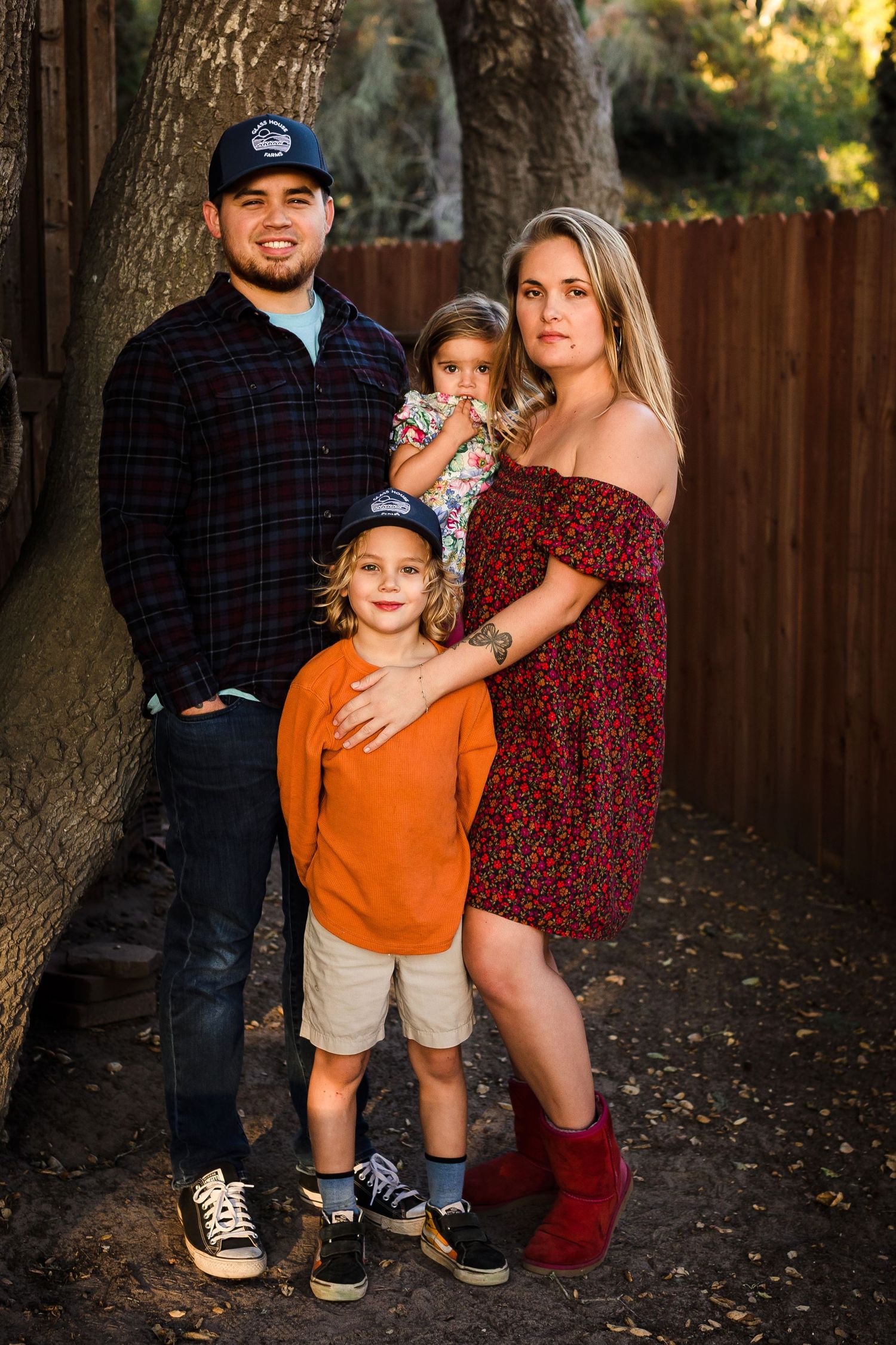 Family poses together outdoors during autumn photo session along wooden fence and fall foliage path.