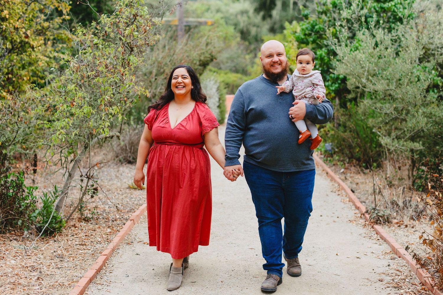 A couple walking together on a tree-lined path wearing red and blue outfits during an outdoor photo session.