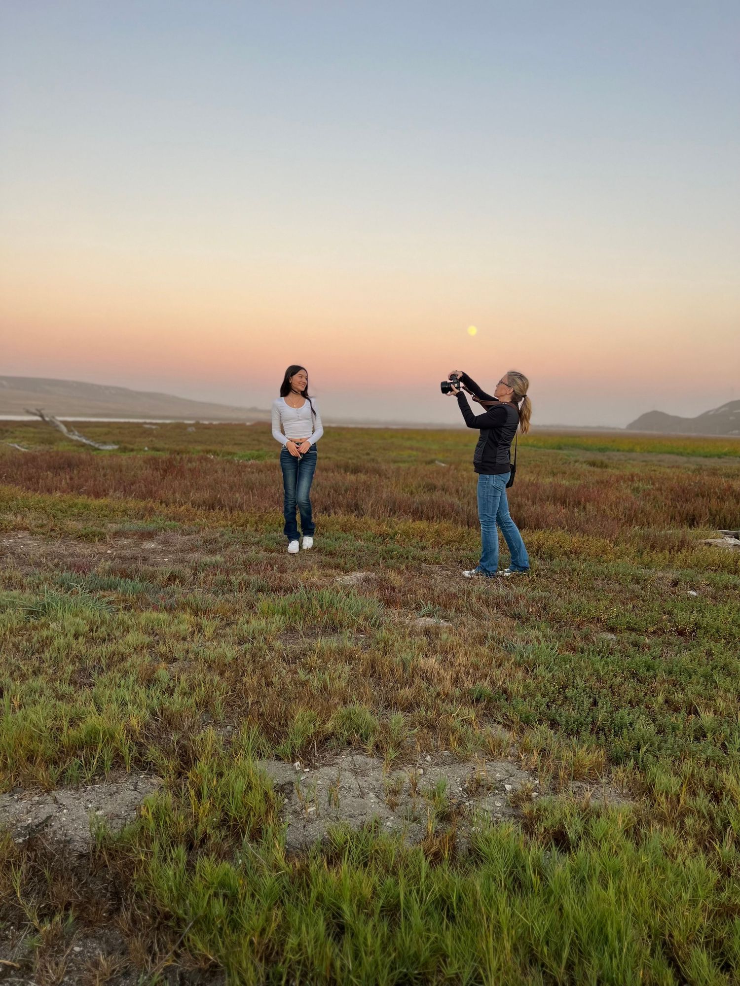 Photographer capturing a woman posing in a coastal marsh during a stunning pink moonrise sunset.