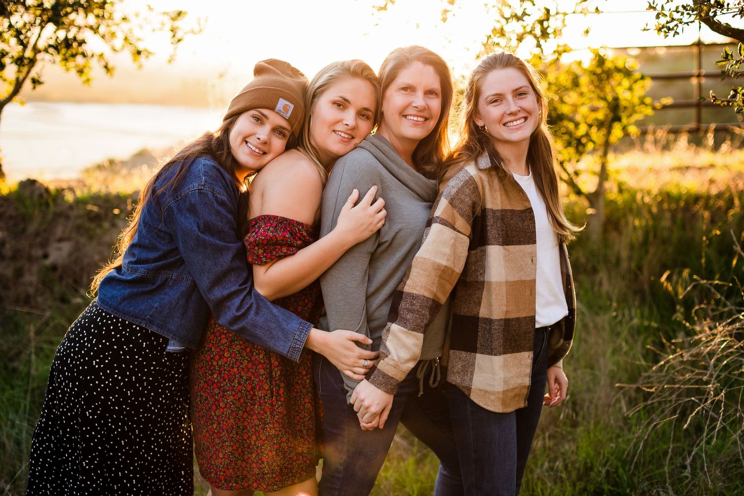 A group of friends laugh together during a warm sunset photoshoot in a rustic outdoor setting.