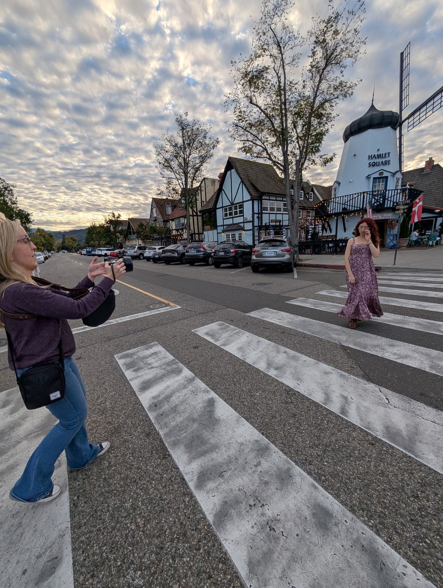 Woman photographing a model in a floral dress on a crosswalk in a charming small town at sunset.