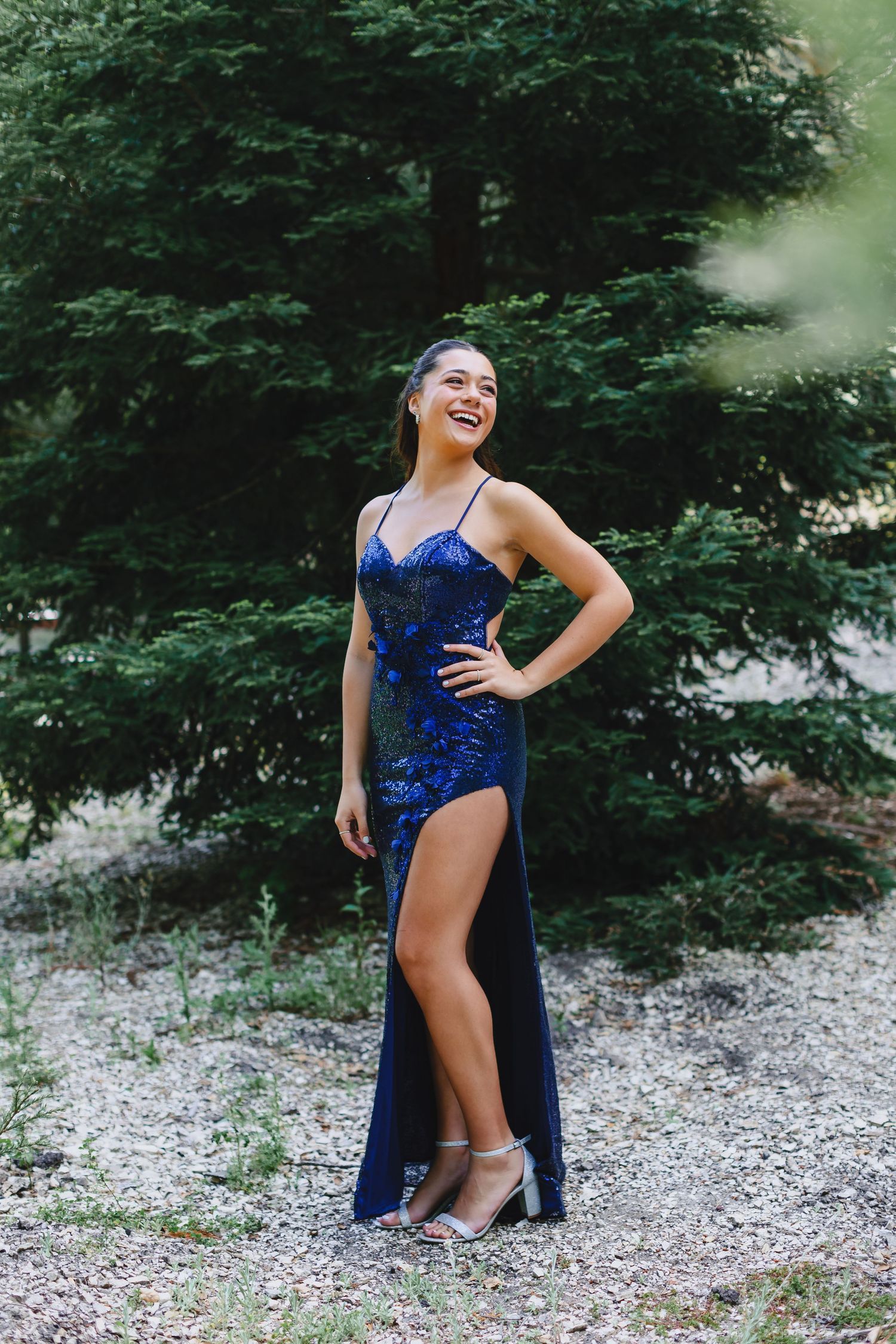 Person in sparkling blue formal dress posing outdoors with trees in background.