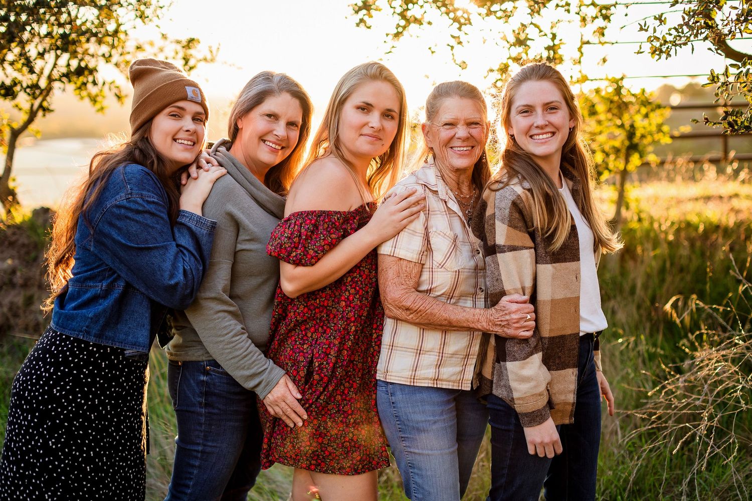 Group of friends pose together outdoors during golden hour sunset in a natural field setting.