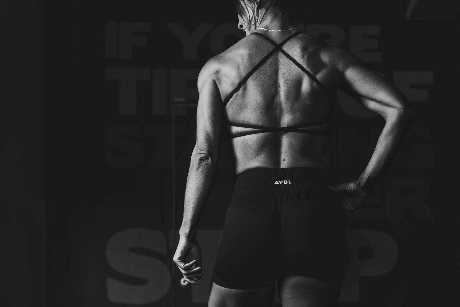 Athletic woman in black sports bra and shorts showing muscular back, black and white fitness photography.