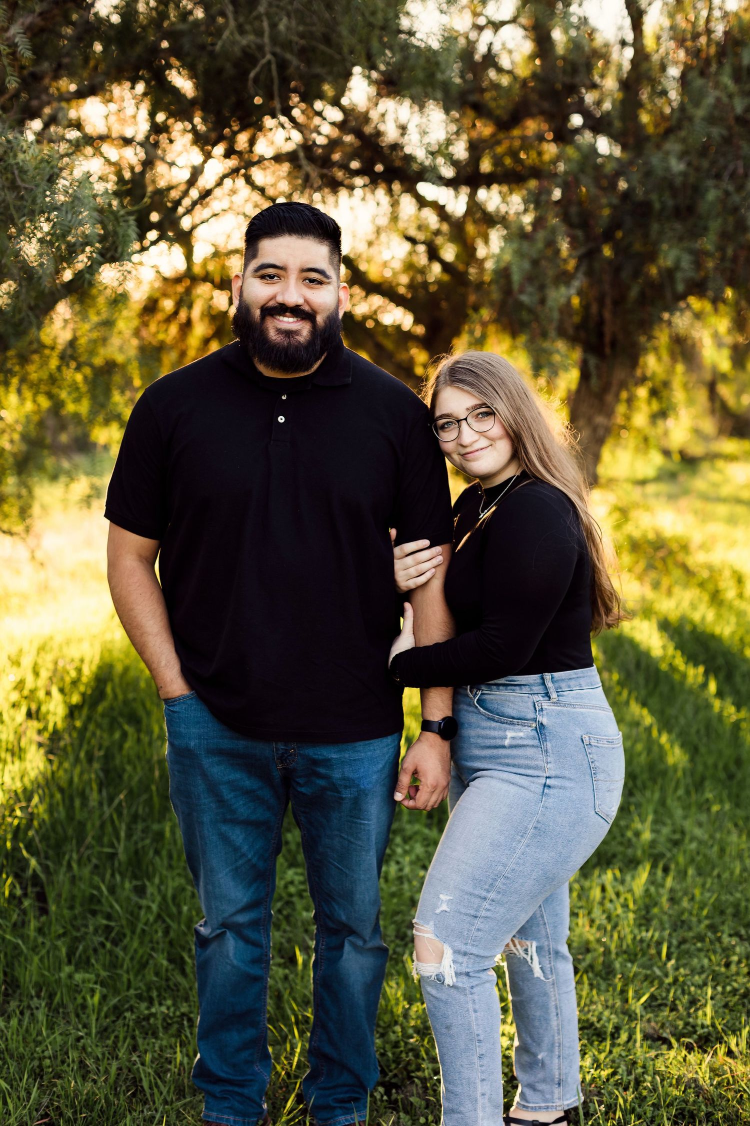 A couple shares tender moments in a sunny field with golden light filtering through trees in the background.