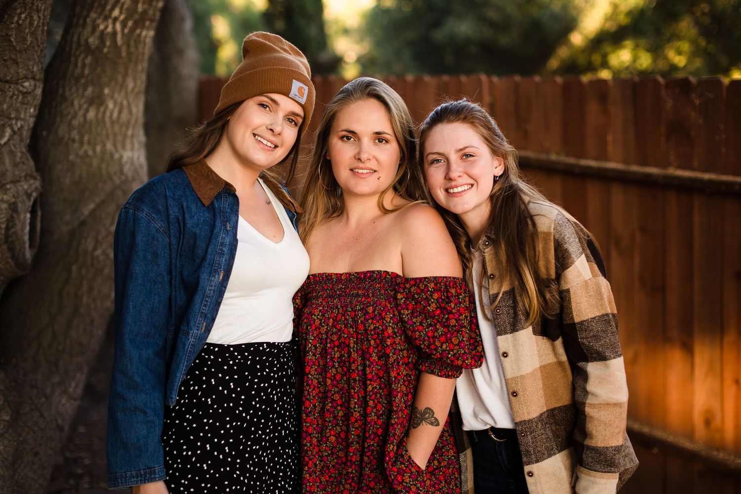 Three people smile outdoors at sunset in a backyard setting with wooden fence in the background.