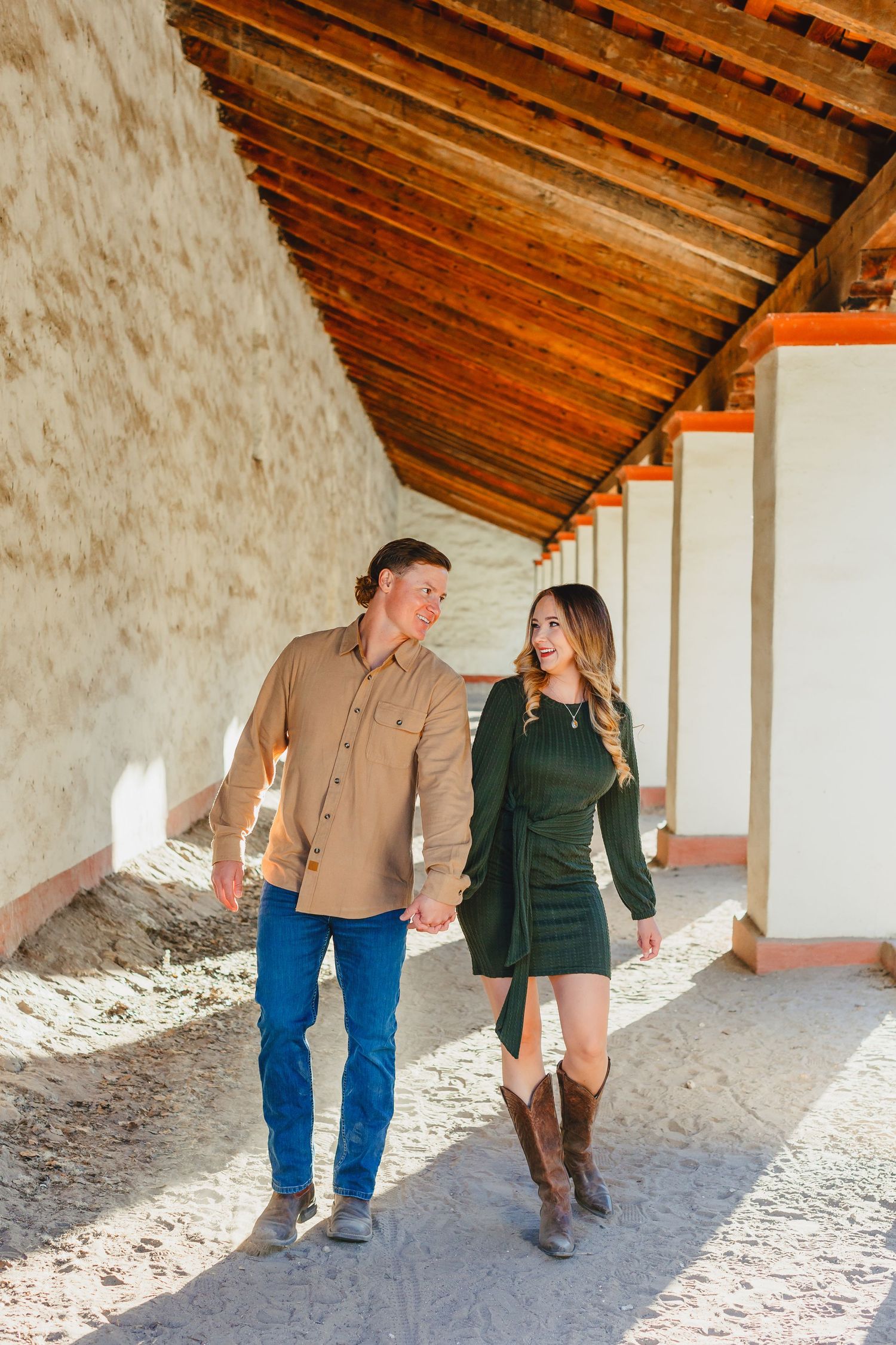 A couple walking together along a covered walkway with wooden beams and rustic architecture.