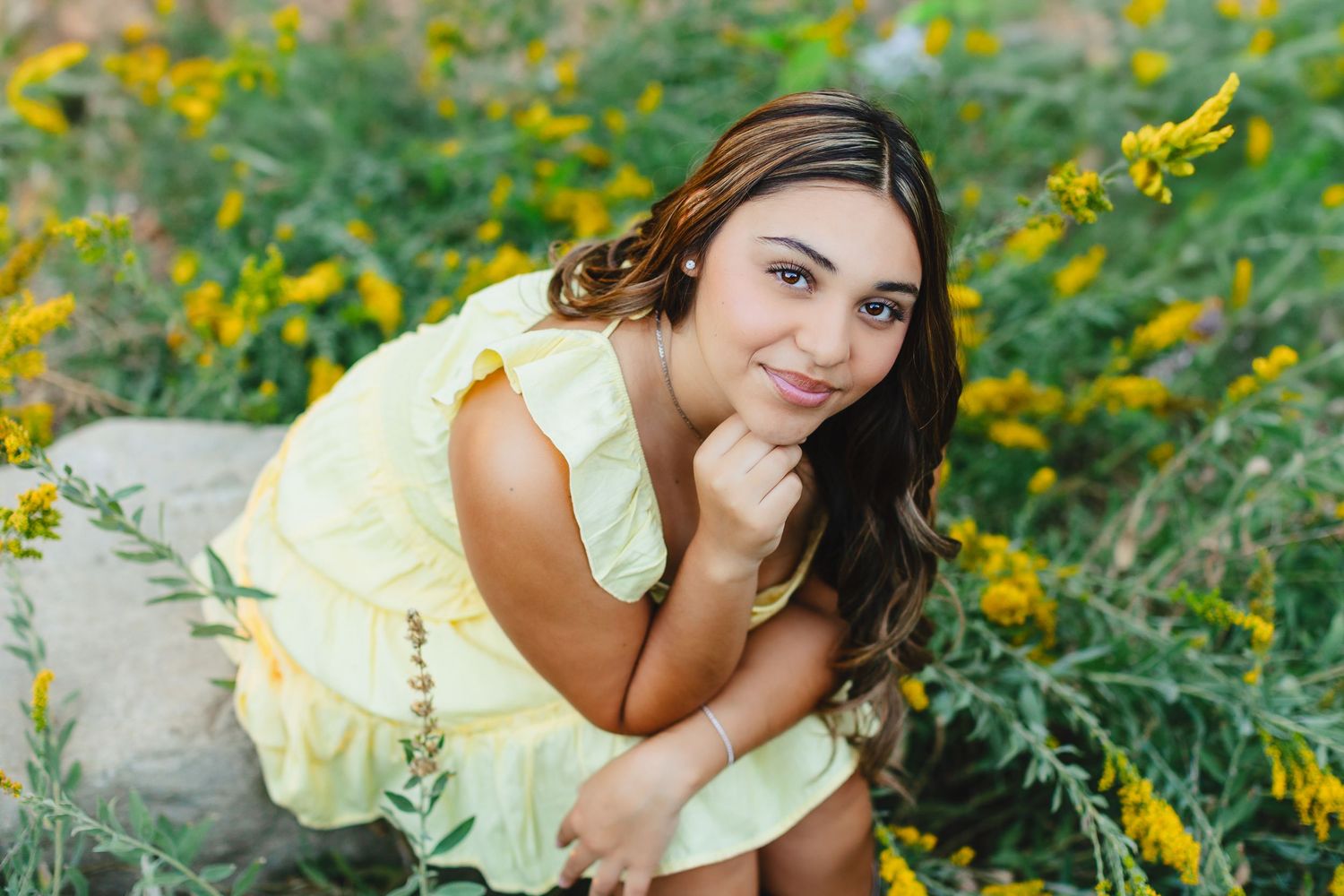 A person in a yellow dress lies among vibrant yellow wildflowers in a sunny meadow.