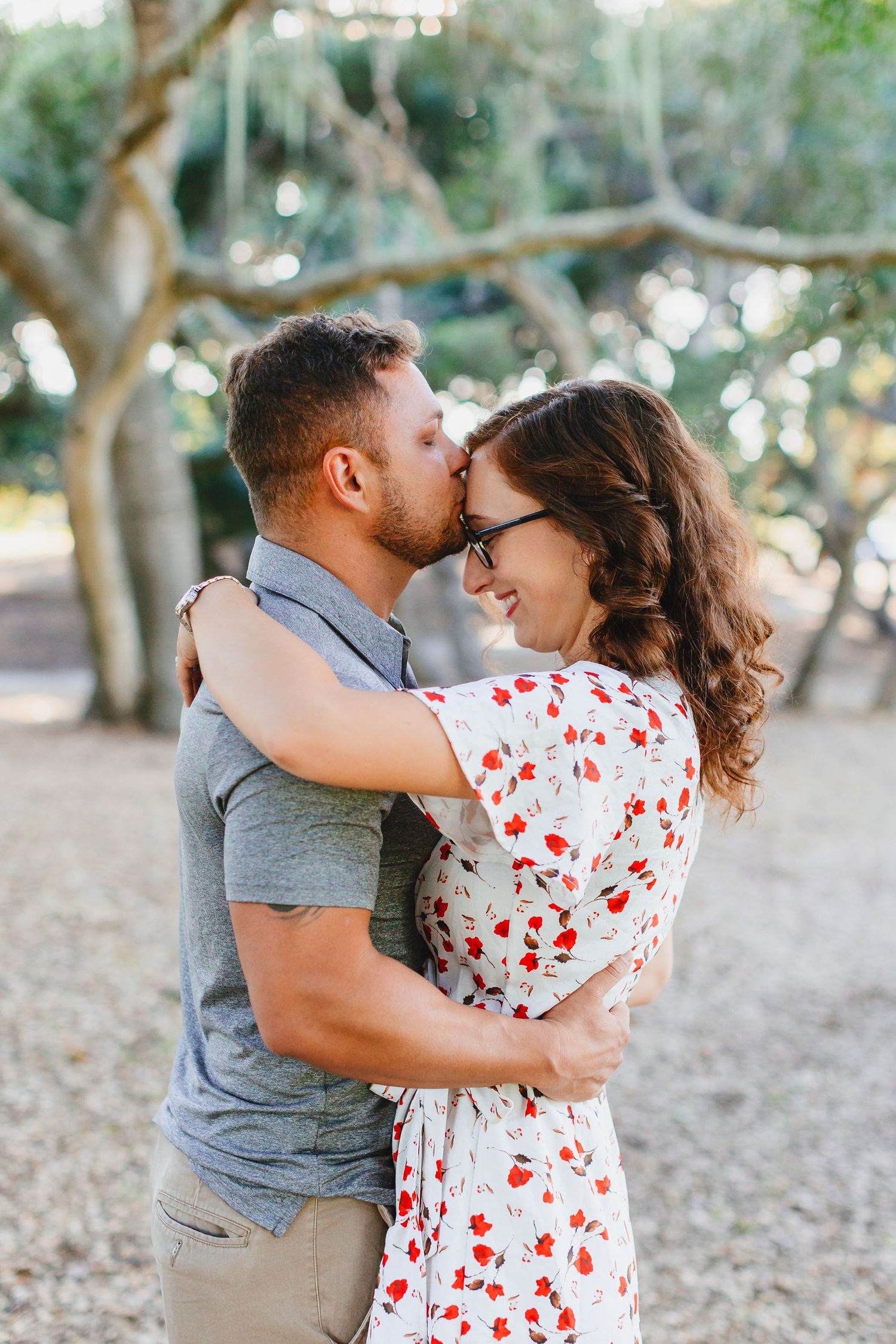 A tender embrace between a couple under trees with dappled sunlight.