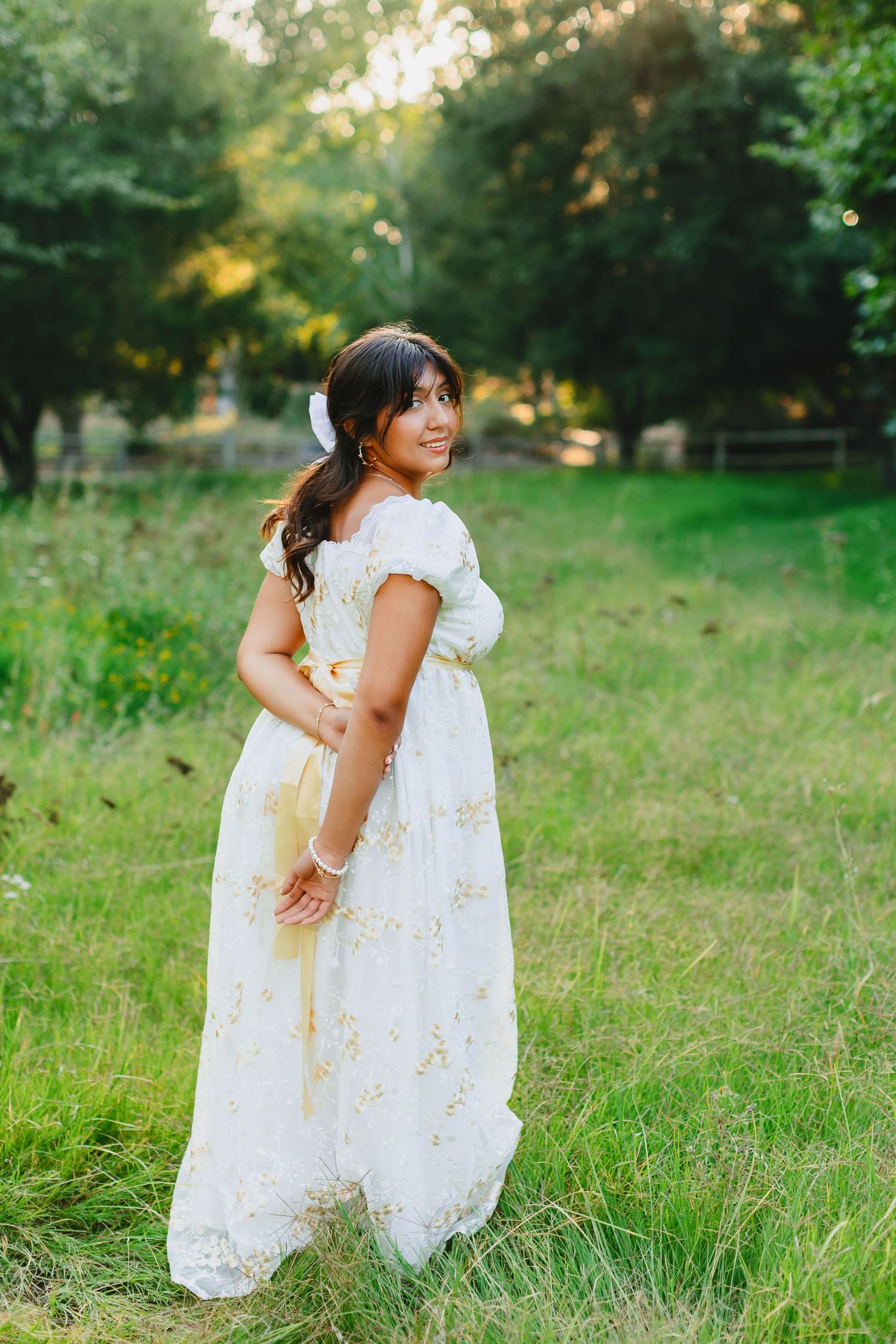 Person in white lace dress standing in grassy field during summer photoshoot.
