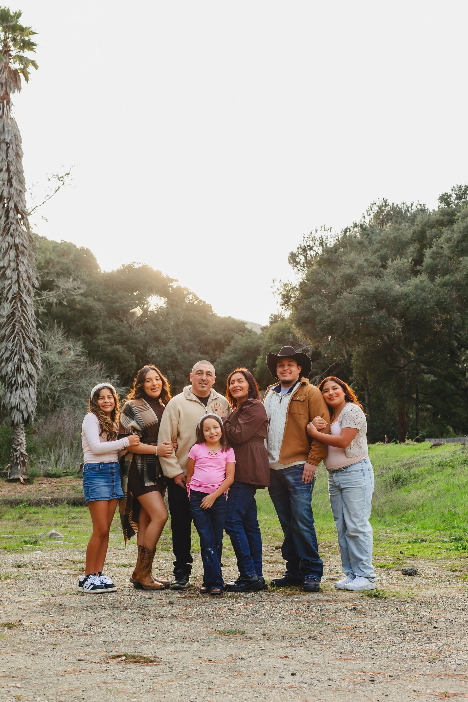 Group of people posing together outdoors at sunset with palm trees in background.