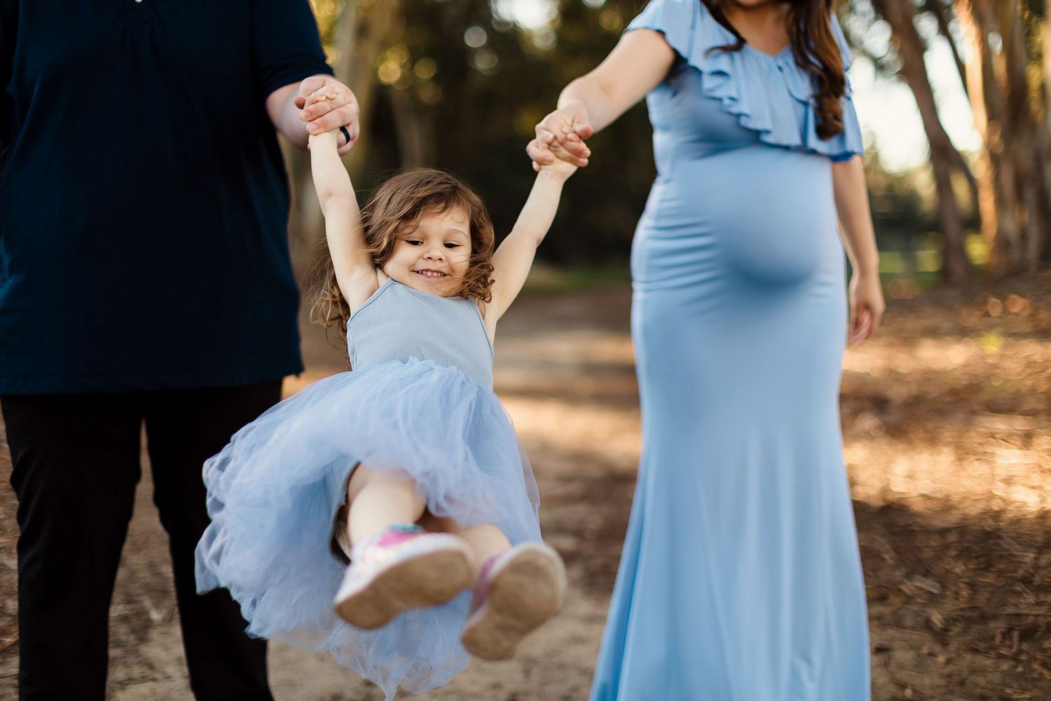 Family enjoys a tender moment in a sun-dappled forest wearing coordinating light blue and white outfits.