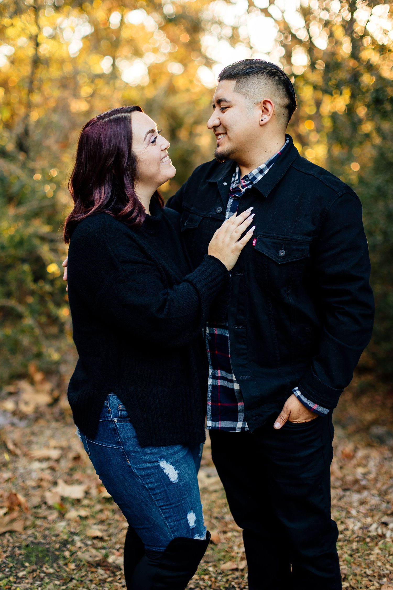 A couple shares an intimate moment outdoors during autumn with golden bokeh lights and fall foliage in the background.