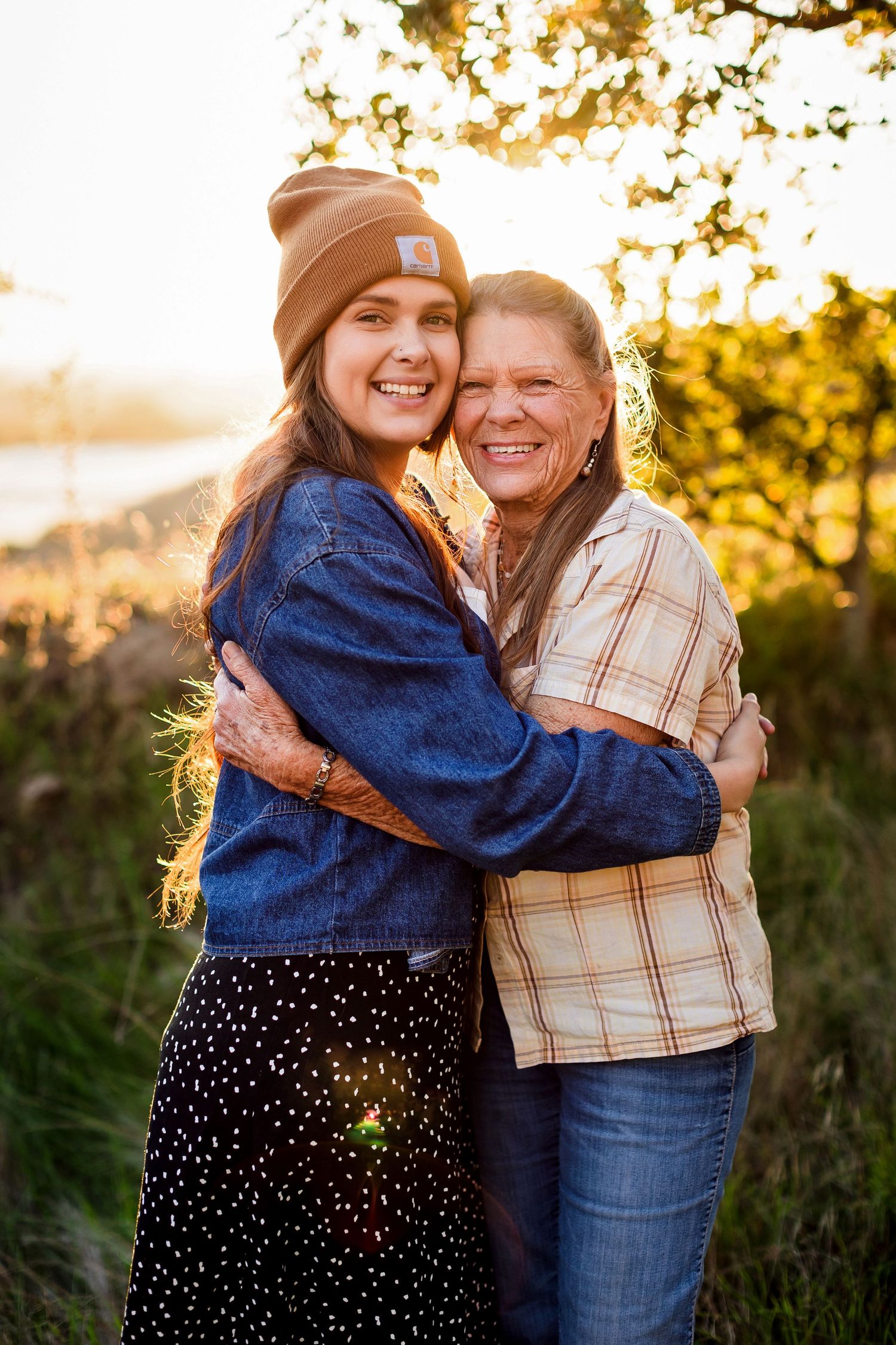 Two people share a joyful embrace outdoors at sunset with golden light filtering through trees in the background.