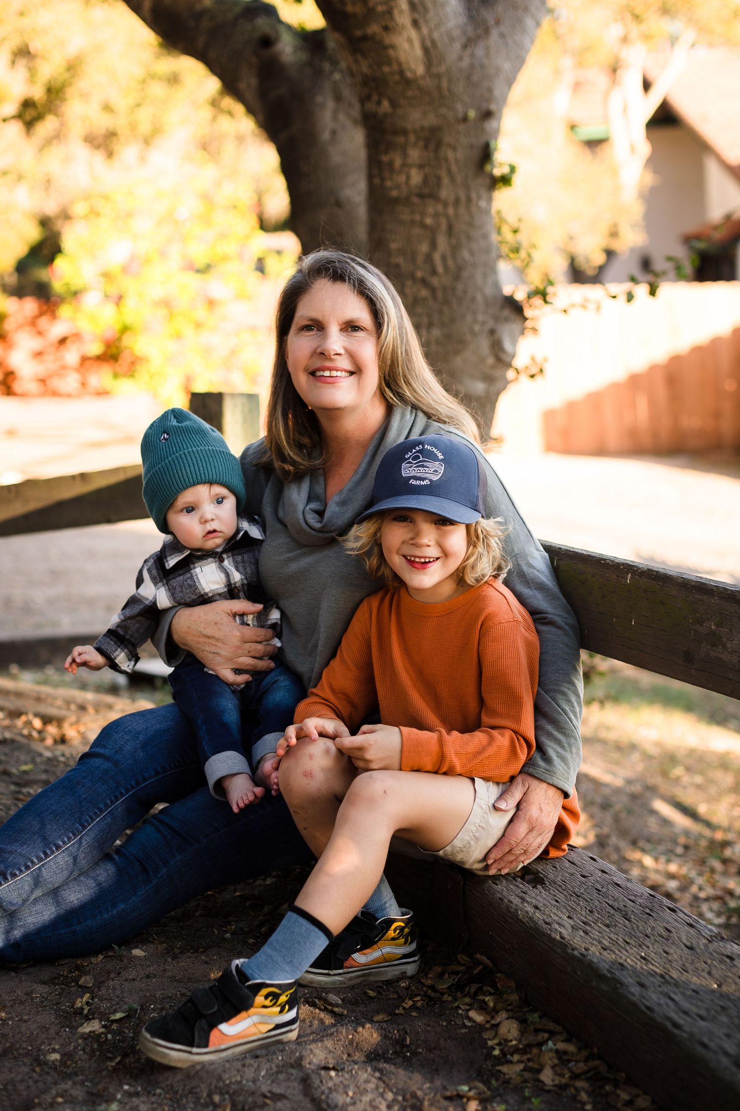 Family relaxing and laughing together on fallen autumn leaves under a large tree.