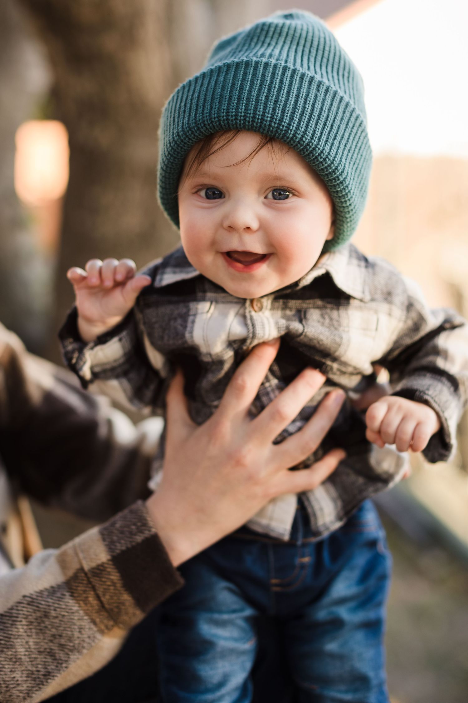 A small child wearing a teal beanie and blue pants holds a cuddly gray and white kitten in a series of sweet photos.