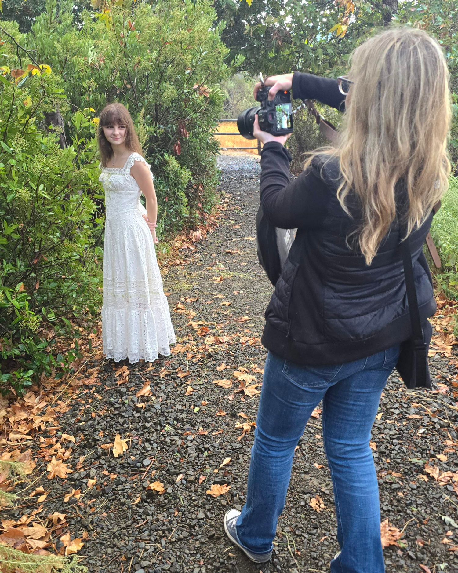 Photographer capturing a young woman in a white dress on a leafy garden path in autumn.