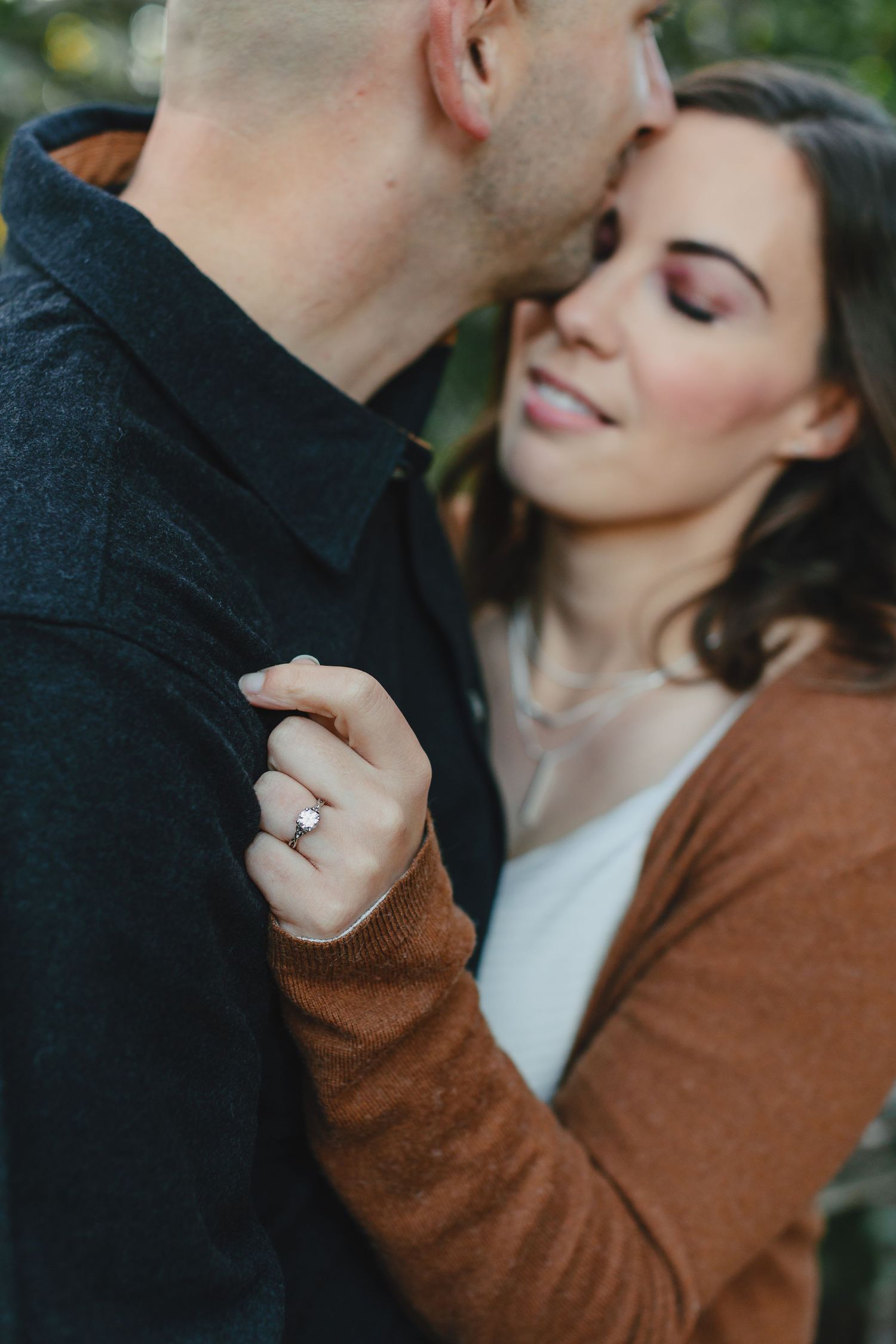 Romantic couple sharing an intimate moment outdoors while showing off engagement ring.