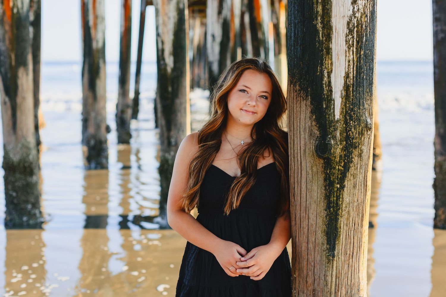 A person poses between wooden pier posts at the beach during sunset, creating a serene coastal portrait.