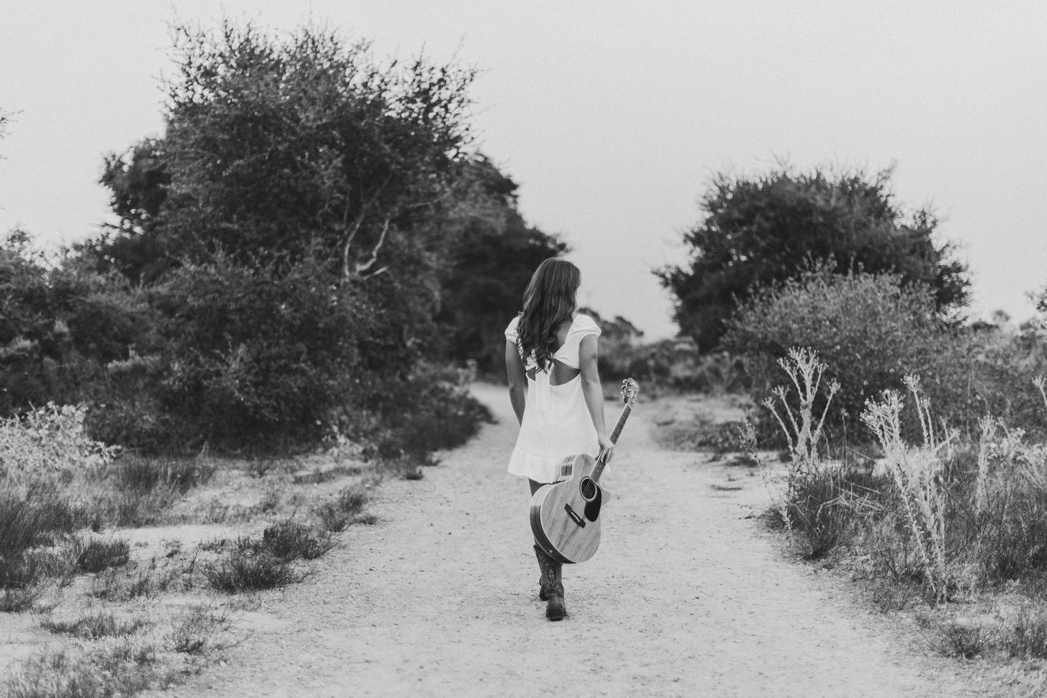 A figure in white walks along a dusty path in black and white photography.