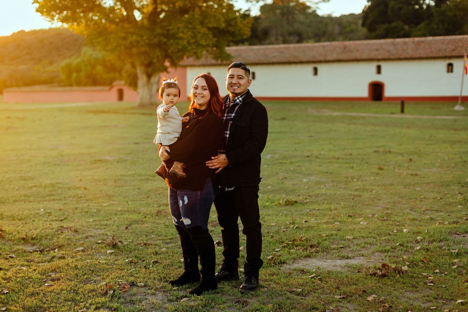 A family stands together on a grassy lawn at sunset with a white building in the background.