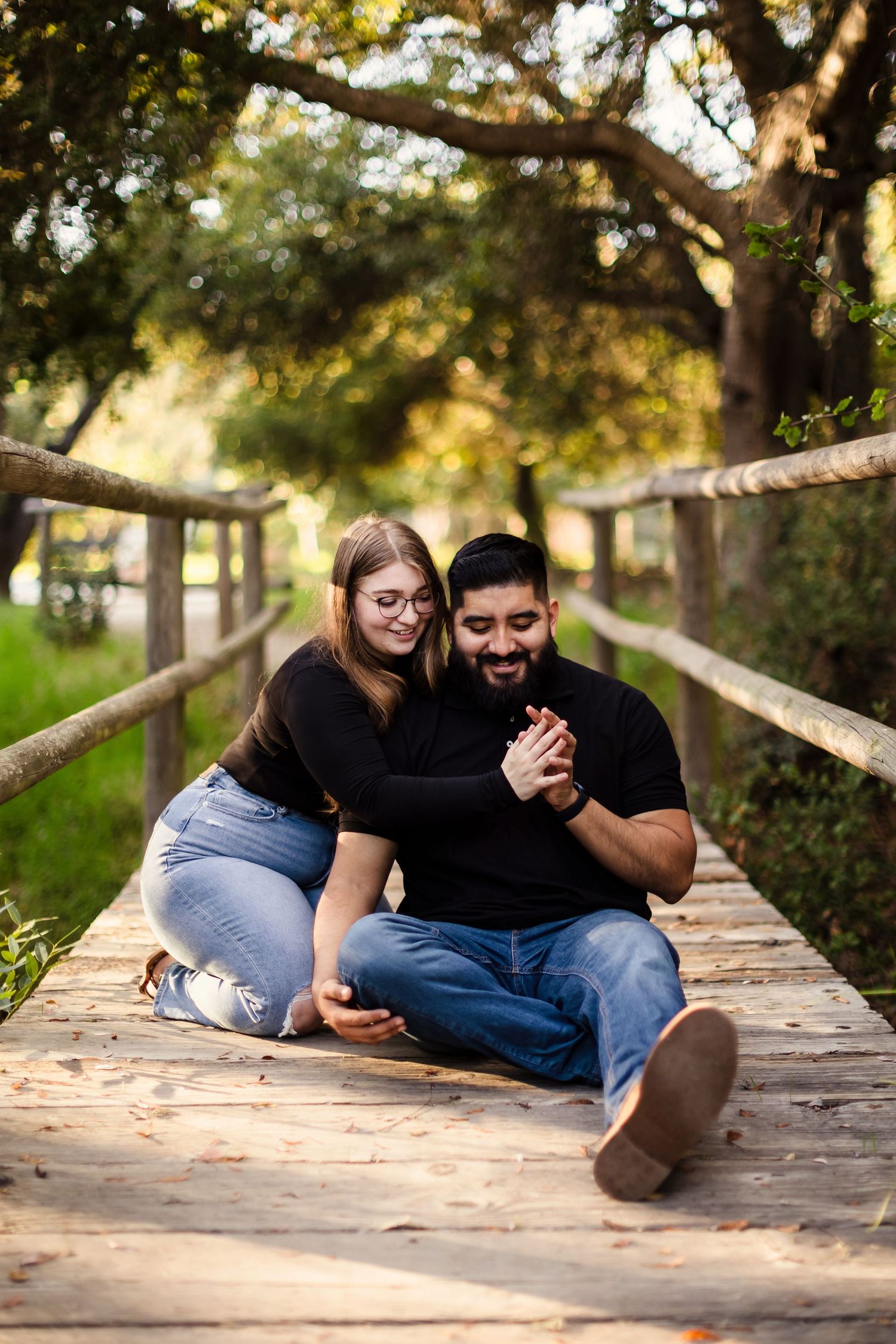 A couple shares a romantic moment lying together on a wooden boardwalk in a natural outdoor setting.