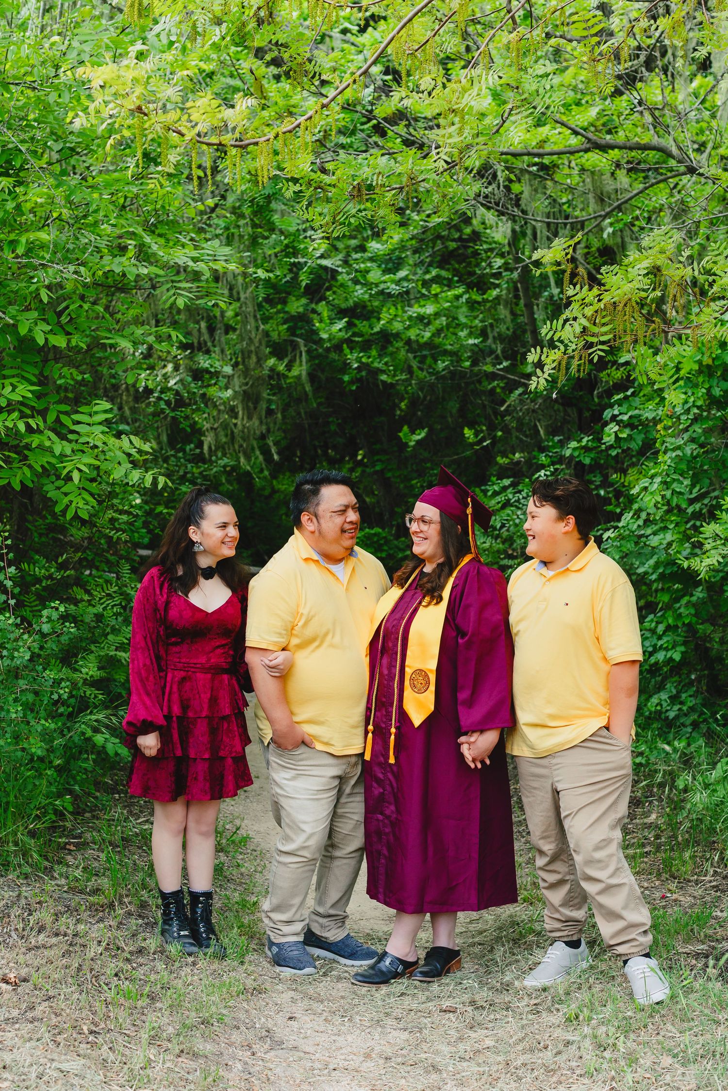 A graduation celebration photo with people wearing burgundy and yellow outfits against green foliage.