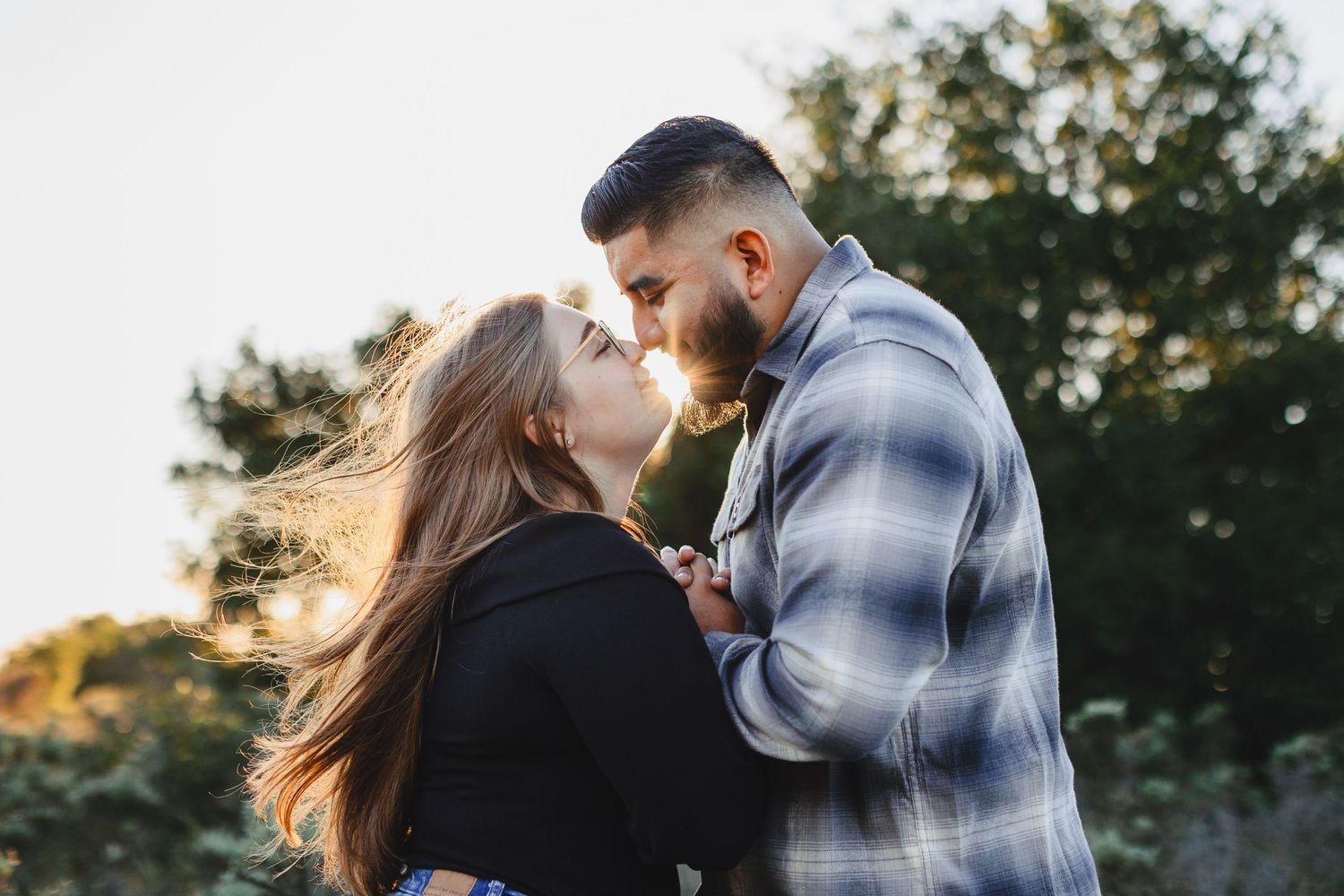 Intimate couple sharing a tender kiss outdoors with soft natural lighting.