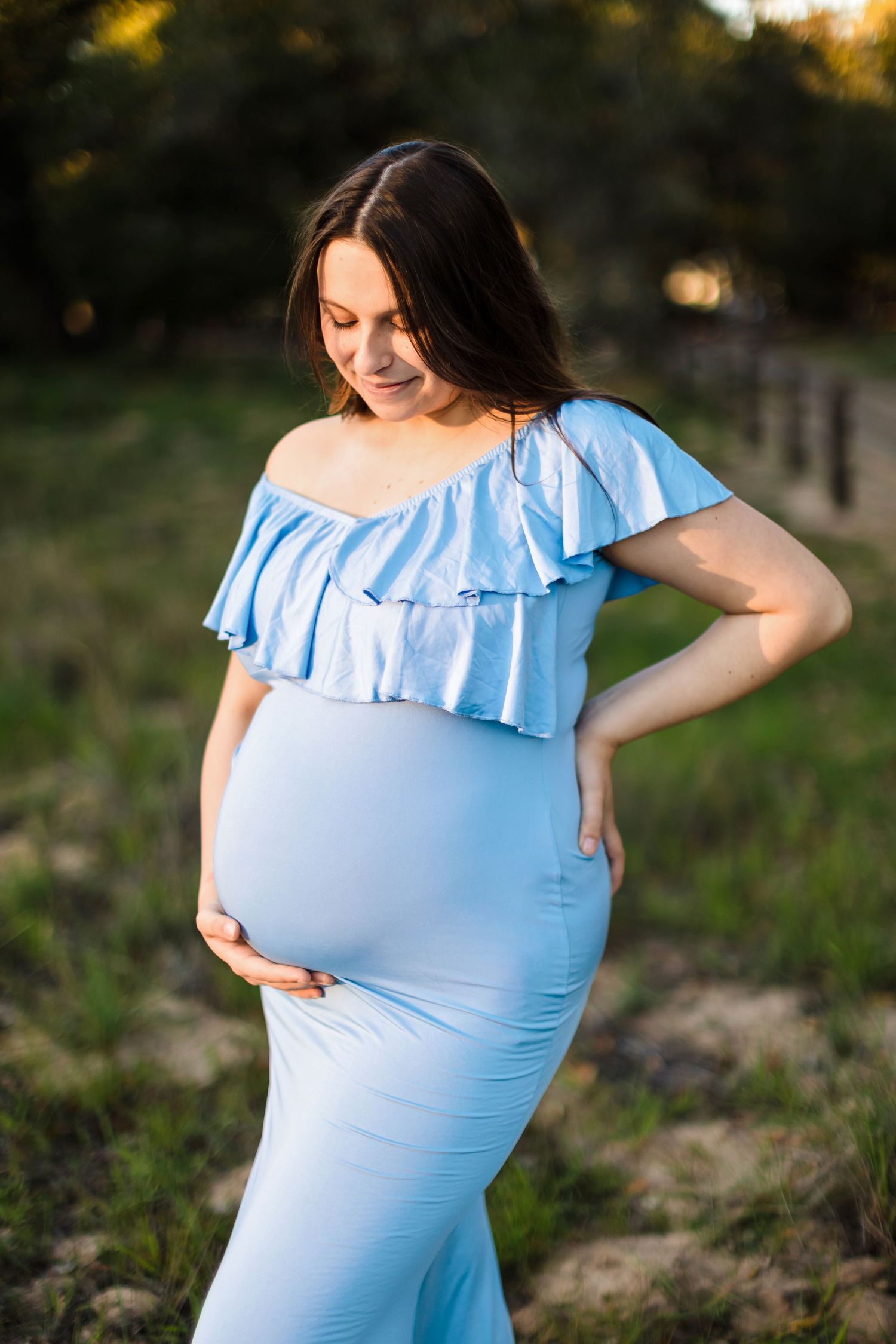 A maternity photoshoot series showing a woman in a light blue ruffled dress standing outdoors at sunset.