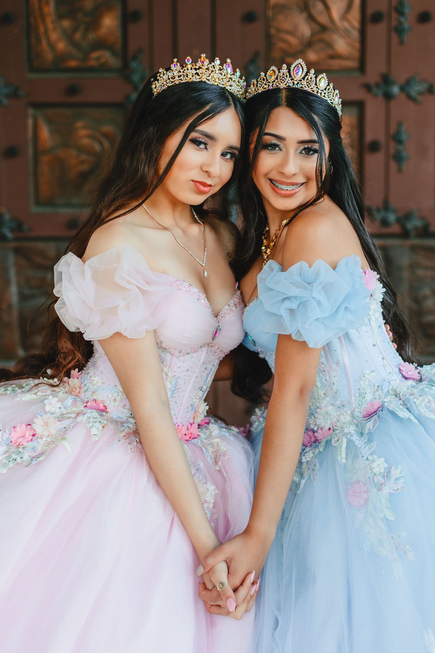 Two friends in princess gowns and tiaras pose together in pink and blue dresses.
