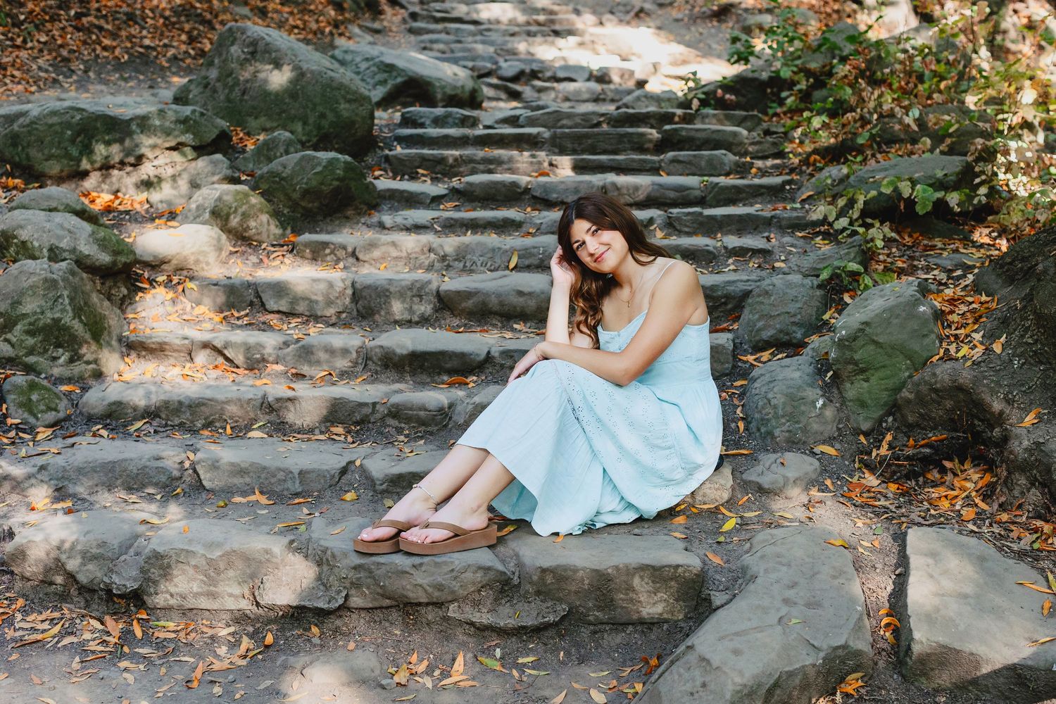 A dreamy outdoor portrait session on rustic stone steps surrounded by autumn foliage and dappled sunlight.